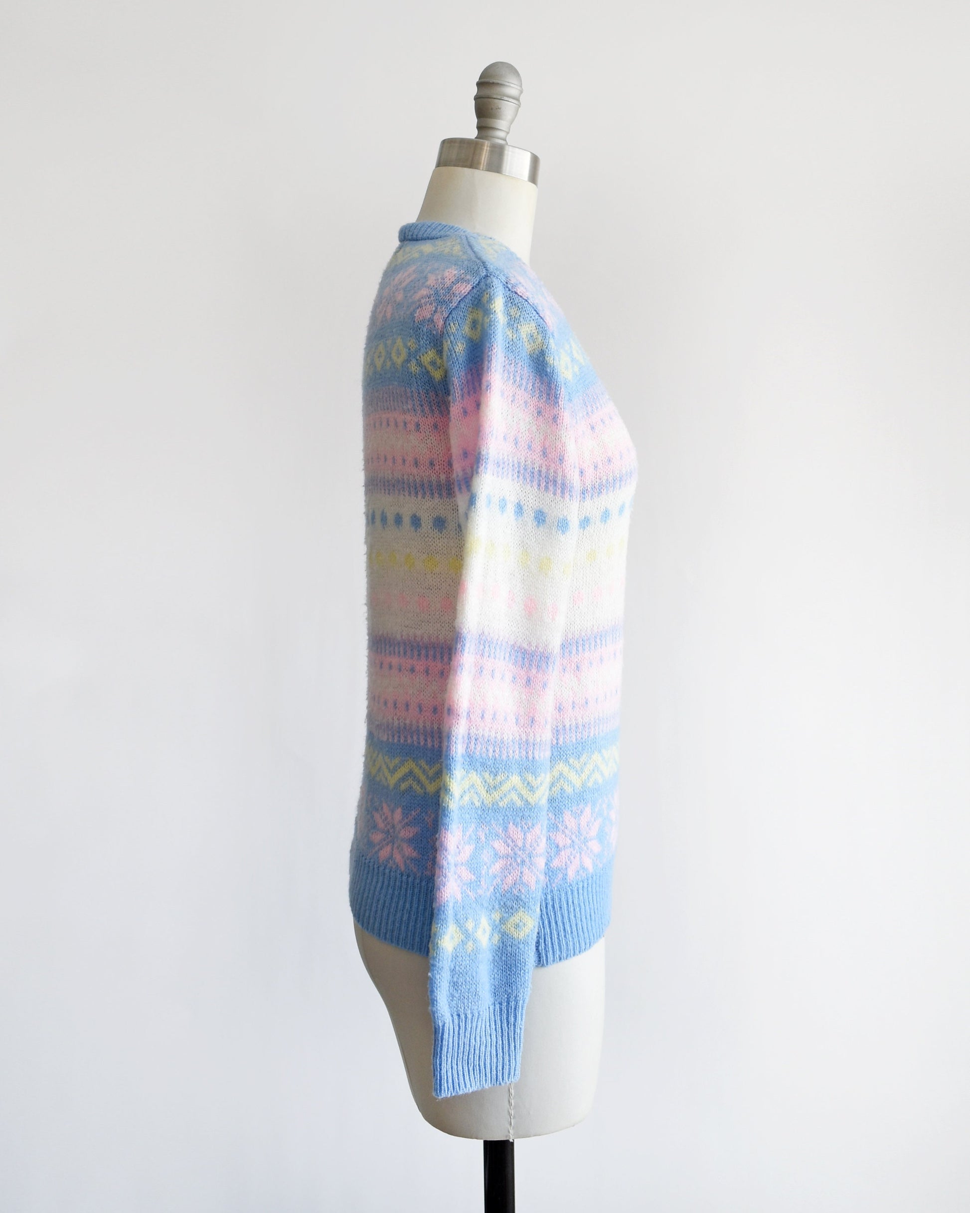 Side view of a vintage 80s pastel striped sweater thats blue, pink, yellow, and white, and at has a snowflake and geometric stripe print on a dress form.