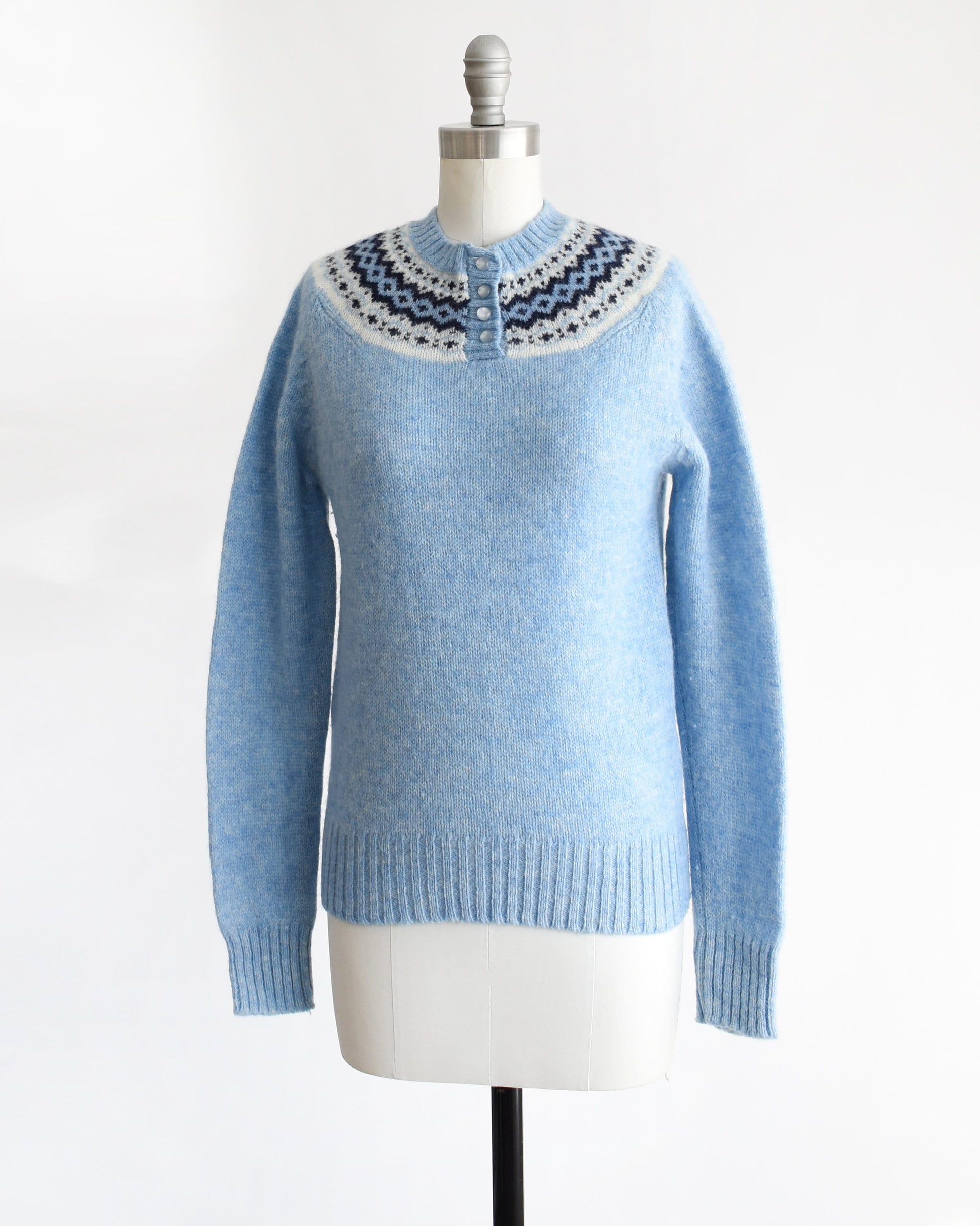 Side front view of a vintage 80s blue sweater with a fair isle pattern around the collar and 4 buttons down the front. The sweater is modeled on a dress form.