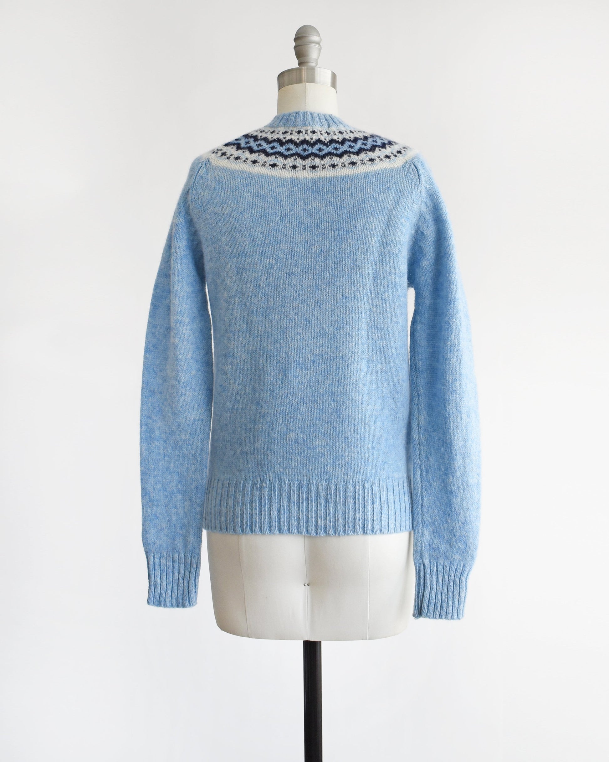 Back view of a vintage 80s blue sweater with a fair isle pattern around the collar. The sweater is modeled on a dress form.