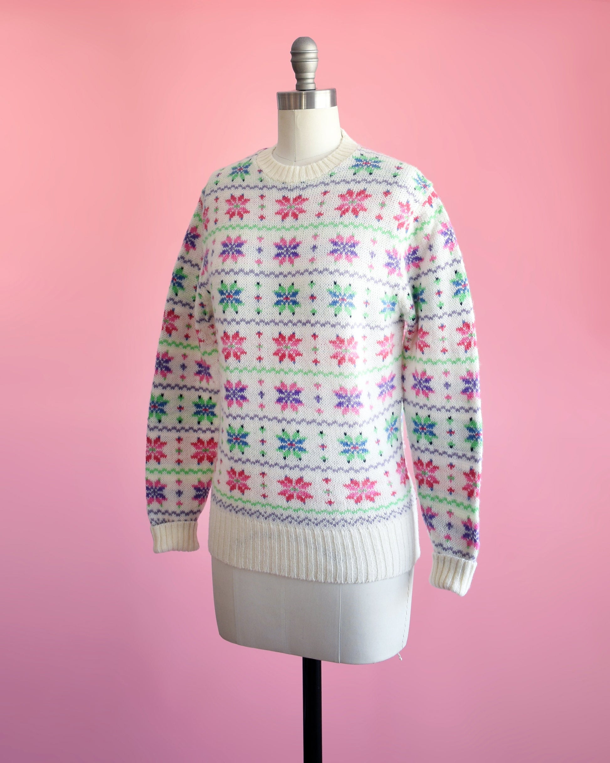 Side front view of a vintage 80s white wool sweater with a green, pink, purple, and blue snowflake pattern on a dress form.