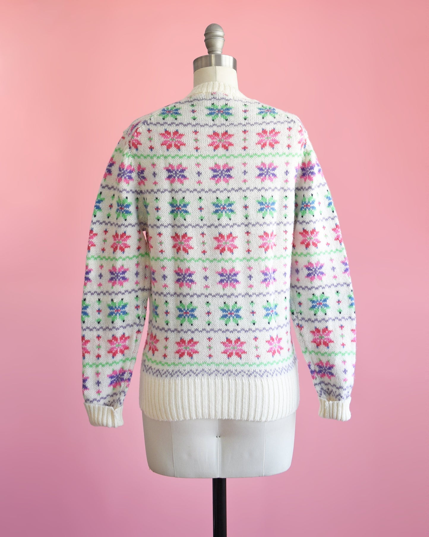 Back view of a vintage 80s white wool sweater with a green, pink, purple, and blue snowflake pattern on a dress form.