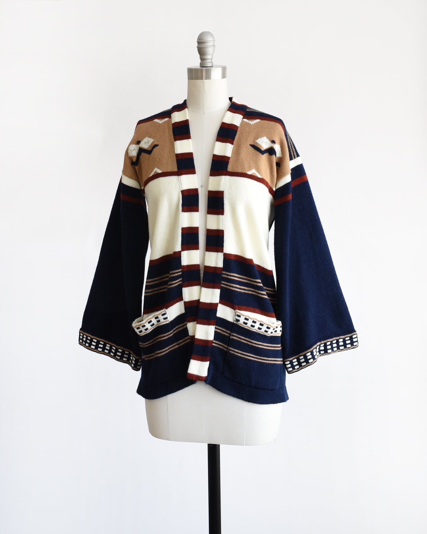 Side front view of a vintage 70s navy blue, tan, reddish brown, and white striped bell sleeve open cardigan on a dress form.