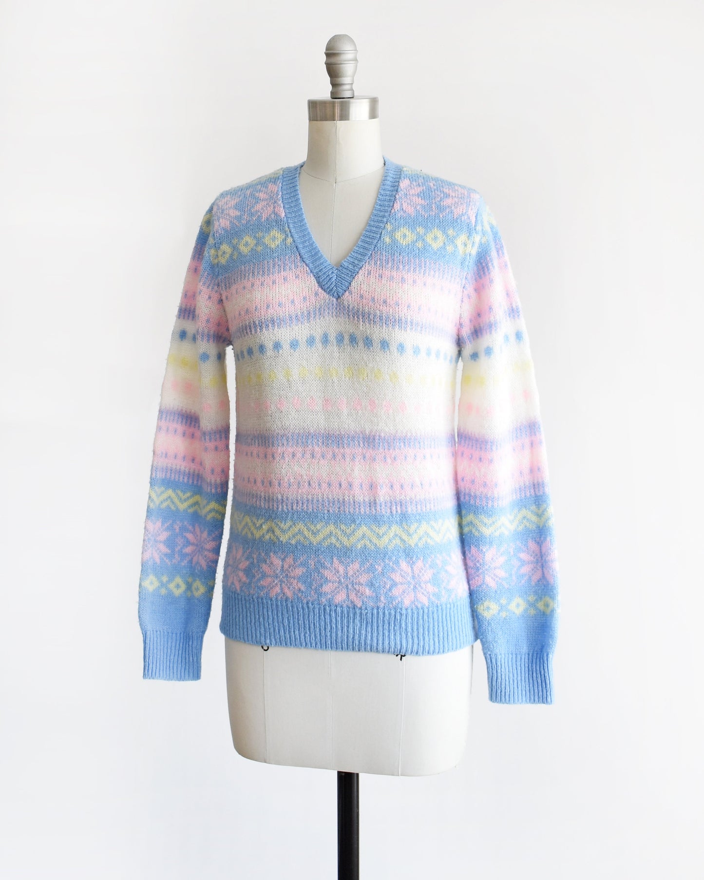 Side front view of a vintage 80s pastel striped sweater thats blue, pink, yellow, and white, and at has a snowflake and geometric stripe print on a dress form.
