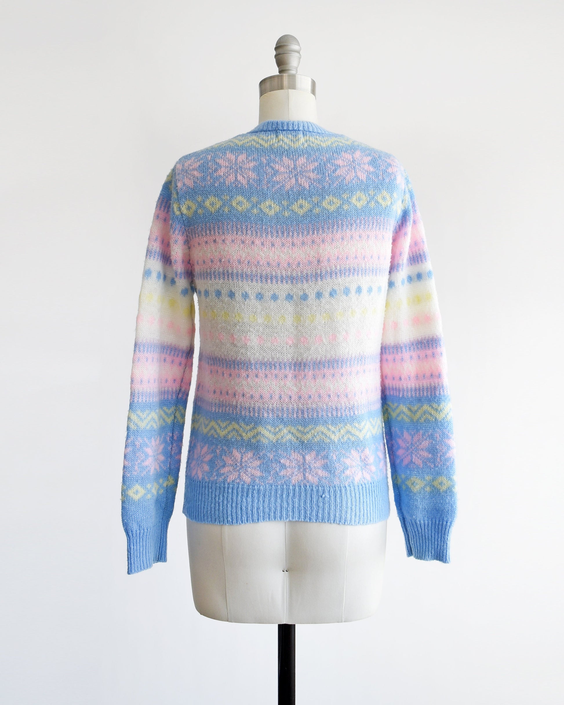 Back view of a vintage 80s pastel striped sweater thats blue, pink, yellow, and white, and at has a snowflake and geometric stripe print on a dress form.