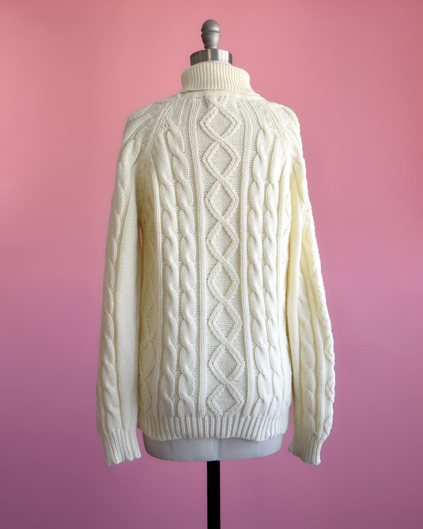 back view of a vintage 70s cream cable knit turtleneck sweater on a dress form set against a pink background