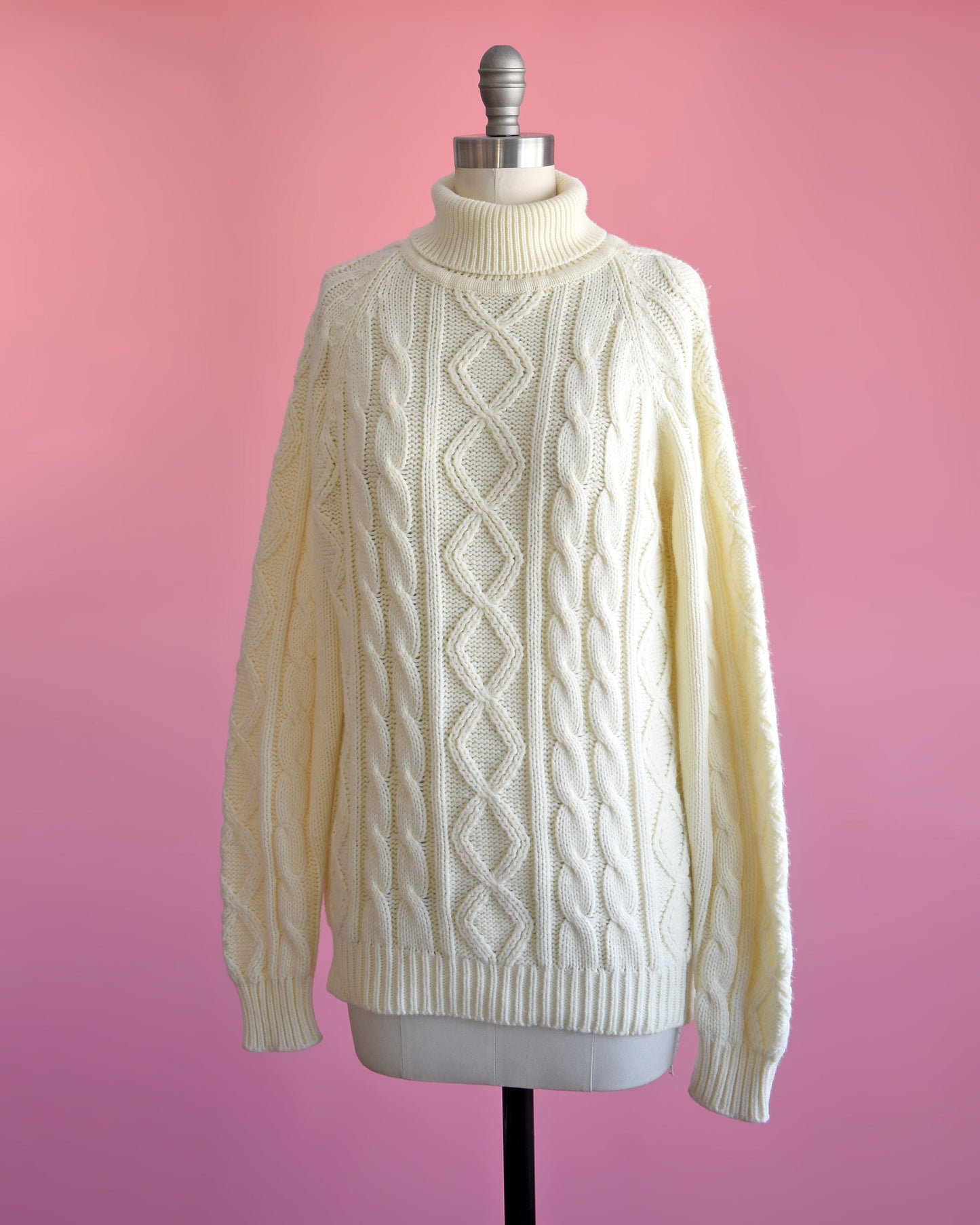side front view of a vintage 70s cream cable knit turtleneck sweater on a dress form set against a pink background