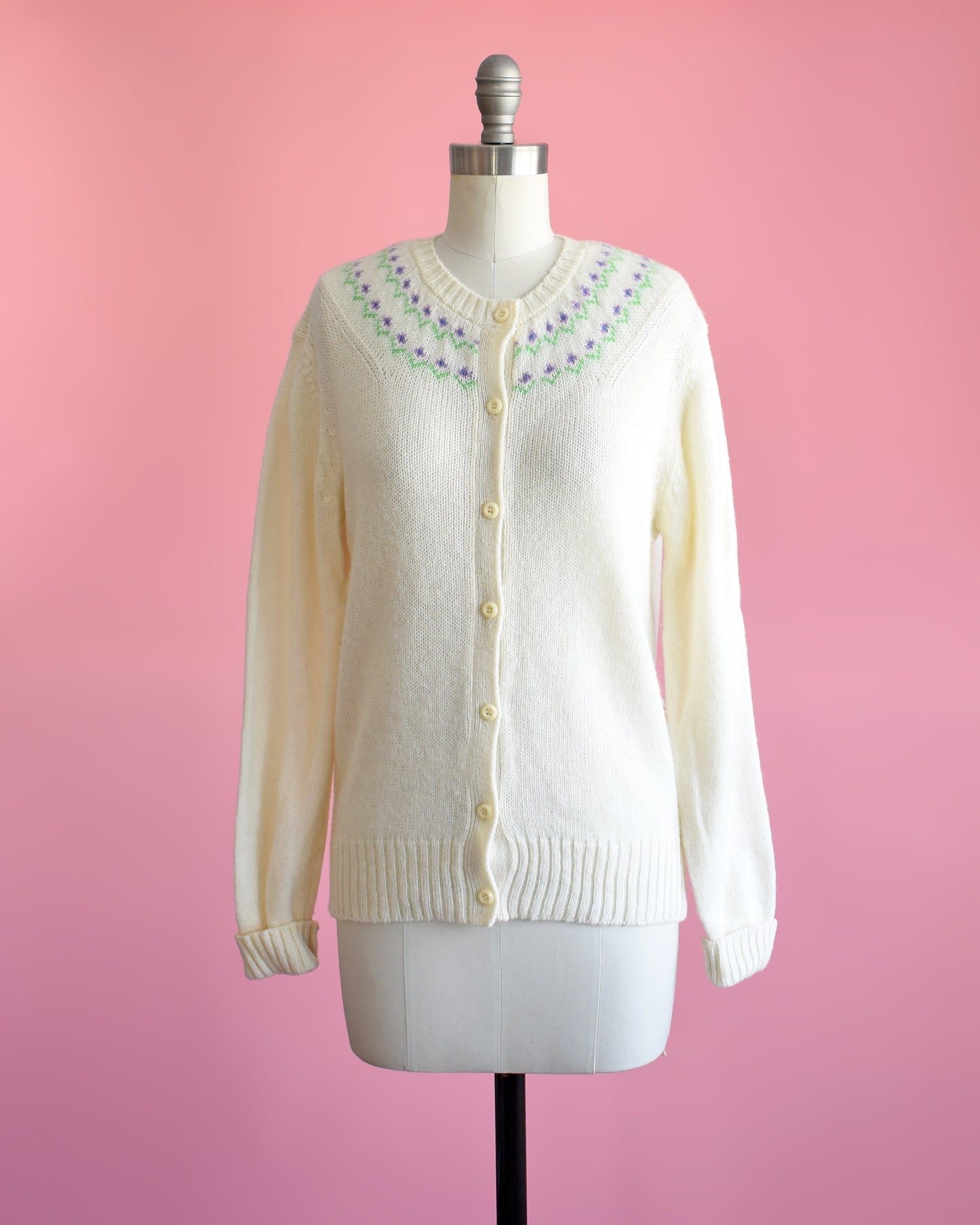 A vintage 70s white cardigan with purple and green flowers around the collar on a dress form.