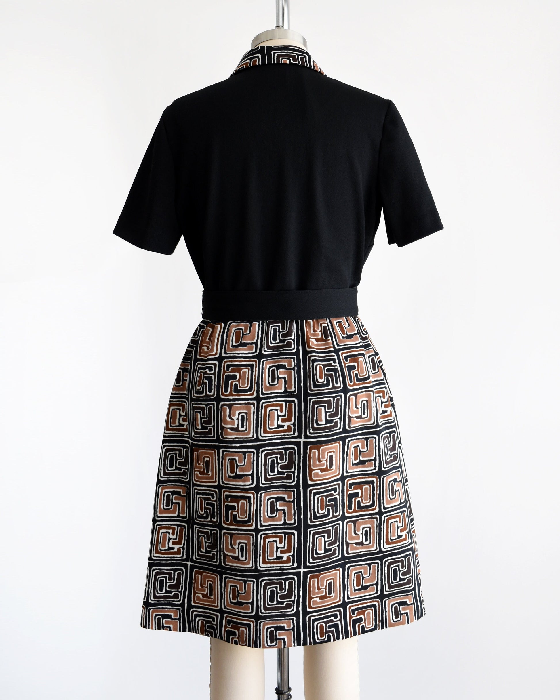 Back view of a vintage 60s dress that has a matching geometric print brown, black and white collar and skirt. Matching black belt. Short sleeves. The dress is on a dress form.