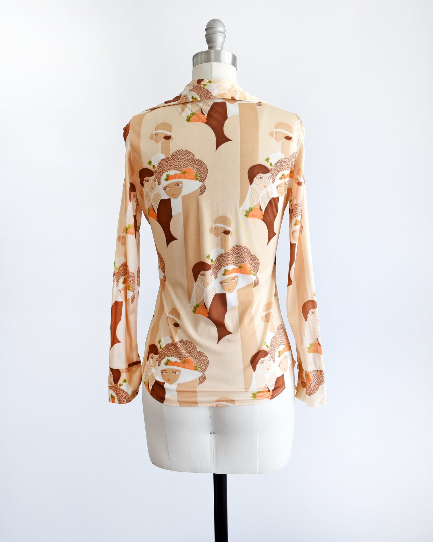 Back view of a vintage 70s blouse that has a novelty print of art deco women faces, along with rectangle shapes, and flowers. The blouse is on a dress form.