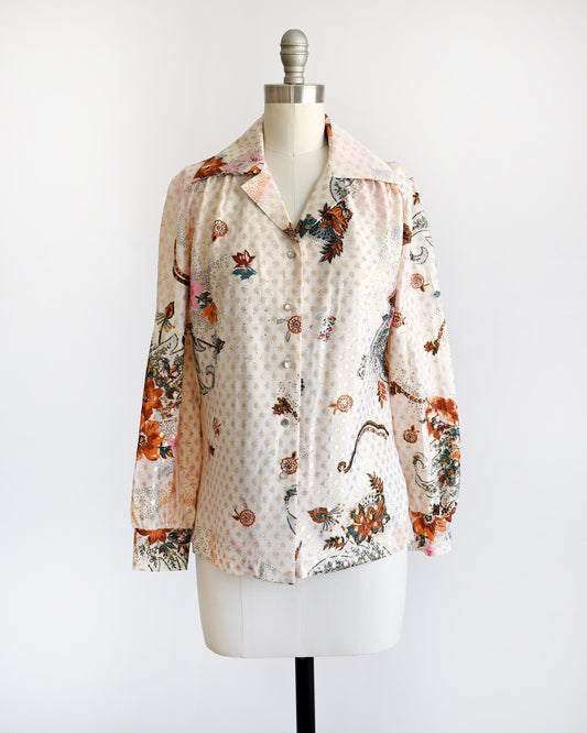 A vintage 70s light cream blouse that has a multicolored floral print and metallic gold connected polka dots all over. Pointy butterfly style collar.  Pearly button up front. The blouse is on a dress form.