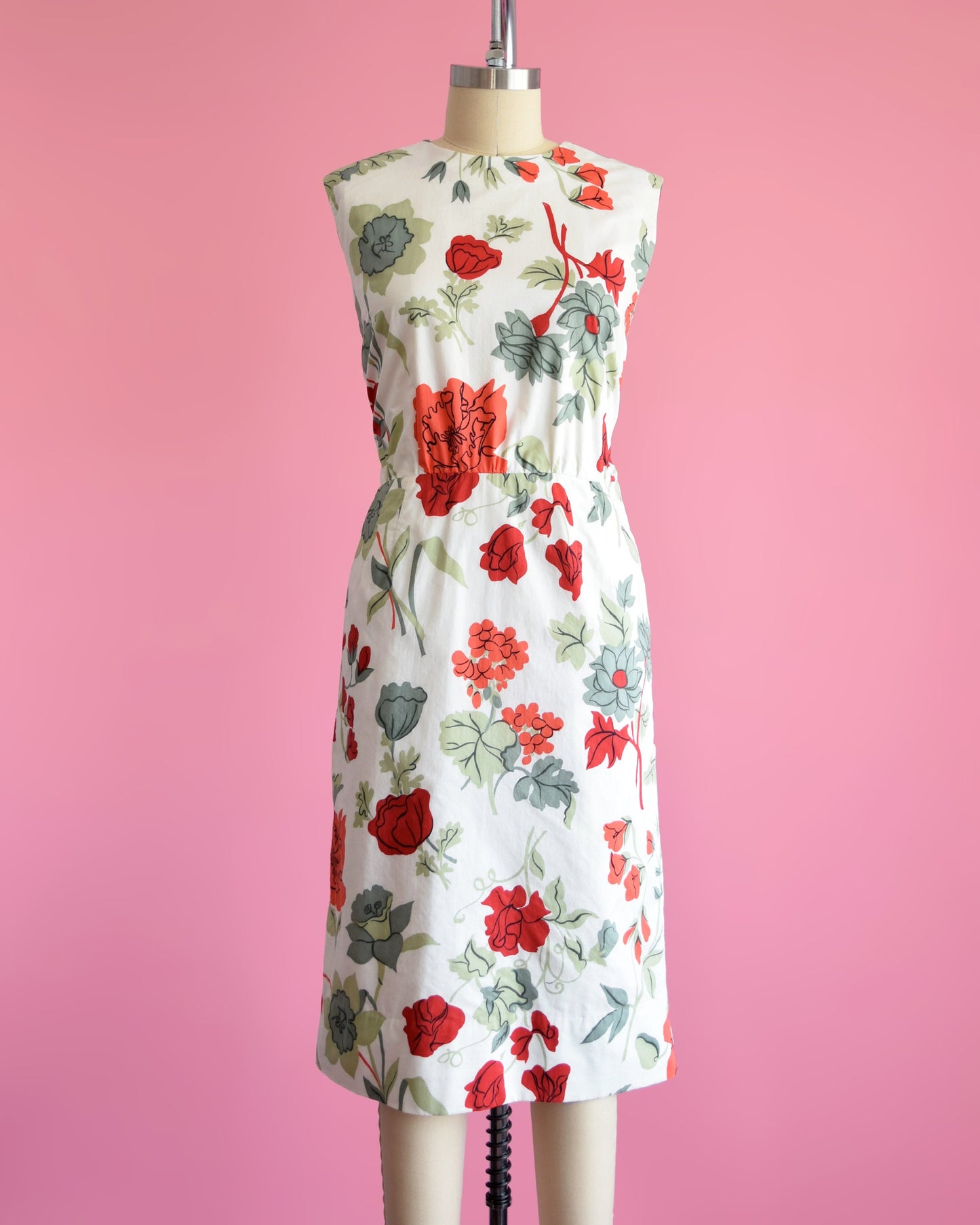 A vintage 60s white dress with a large red and green floral print on a dress form.