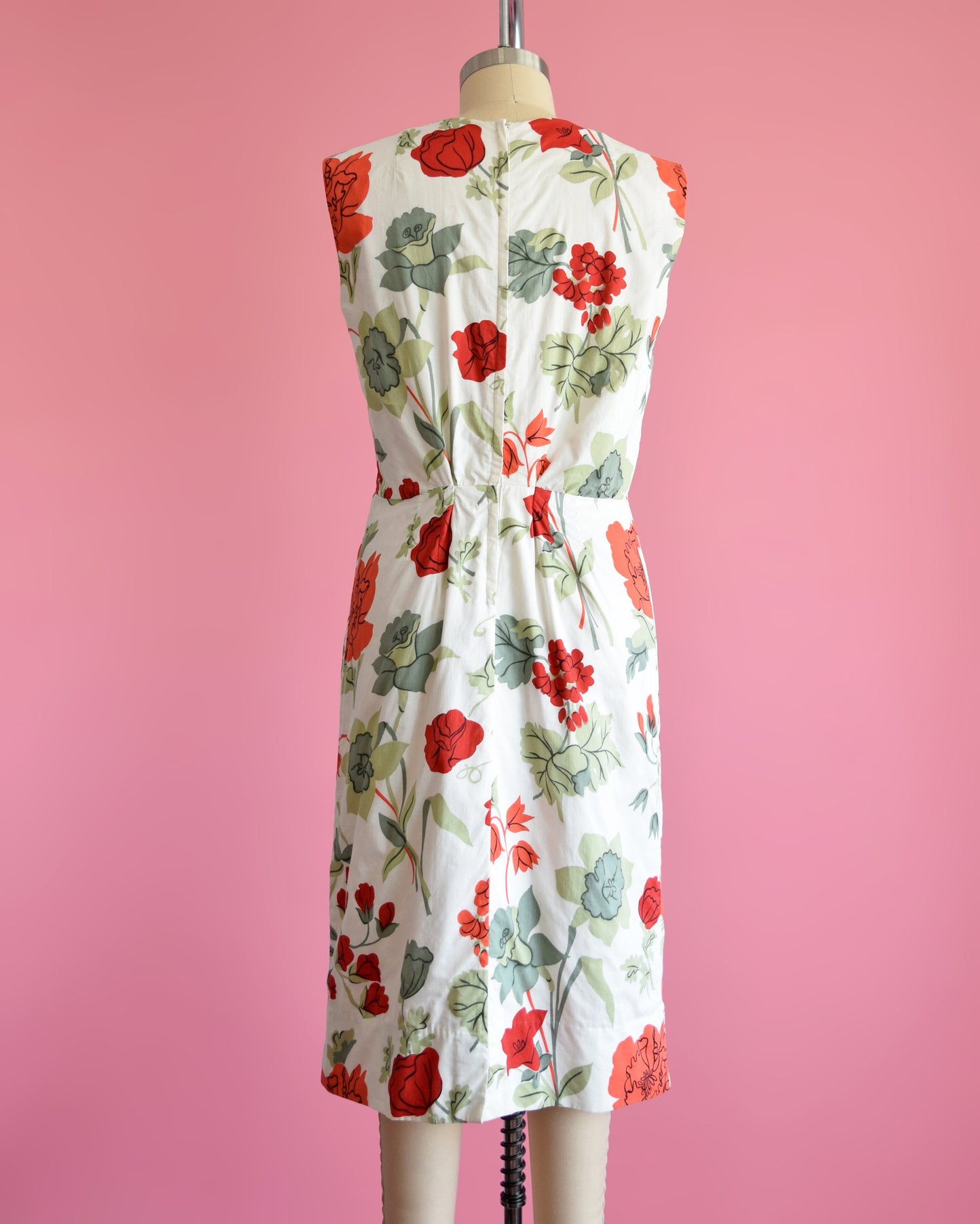 Back view of a vintage 60s white dress with a large red and green floral print on a dress form. The dress has a zipper up the back.