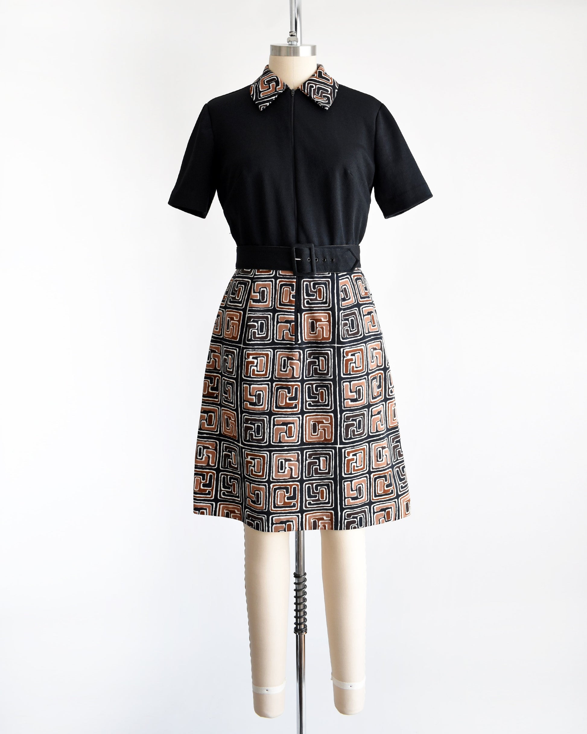 A vintage 60s dress that has a matching geometric print brown, black and white collar and skirt. Zip up front which is zipped down to expose more of the collar. Matching black belt. Short sleeves. The dress is on a dress form.