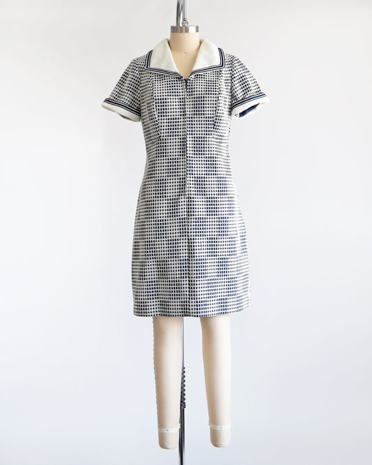 A vintage 70s mod dress that has a blue and white geometric print, white wide collar with navy trim, zip up front, and matching white and navy trim on the short sleeves. The dress is on a dress form.