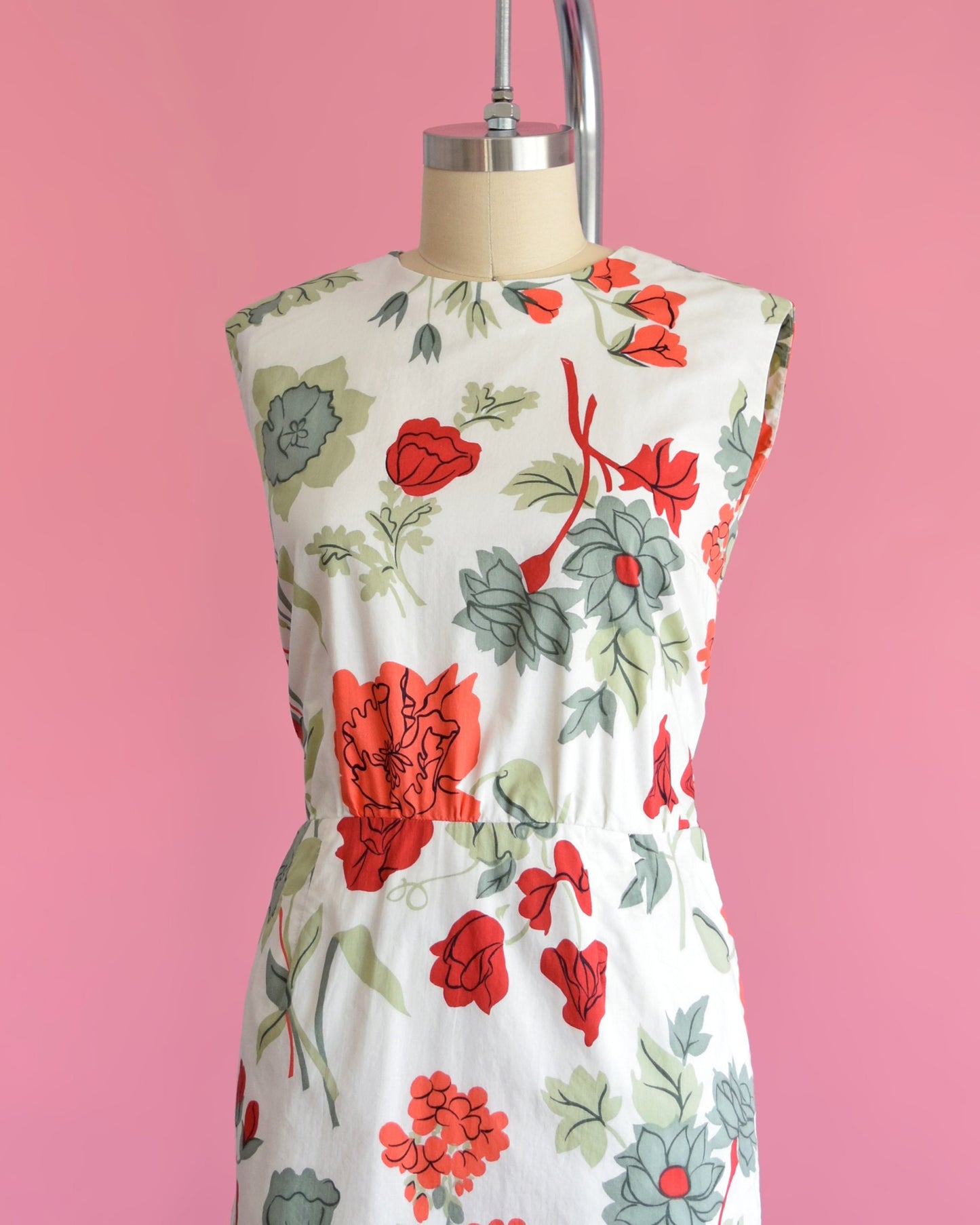 Side front view of a vintage 60s white dress with a large red and green floral print on a dress form.