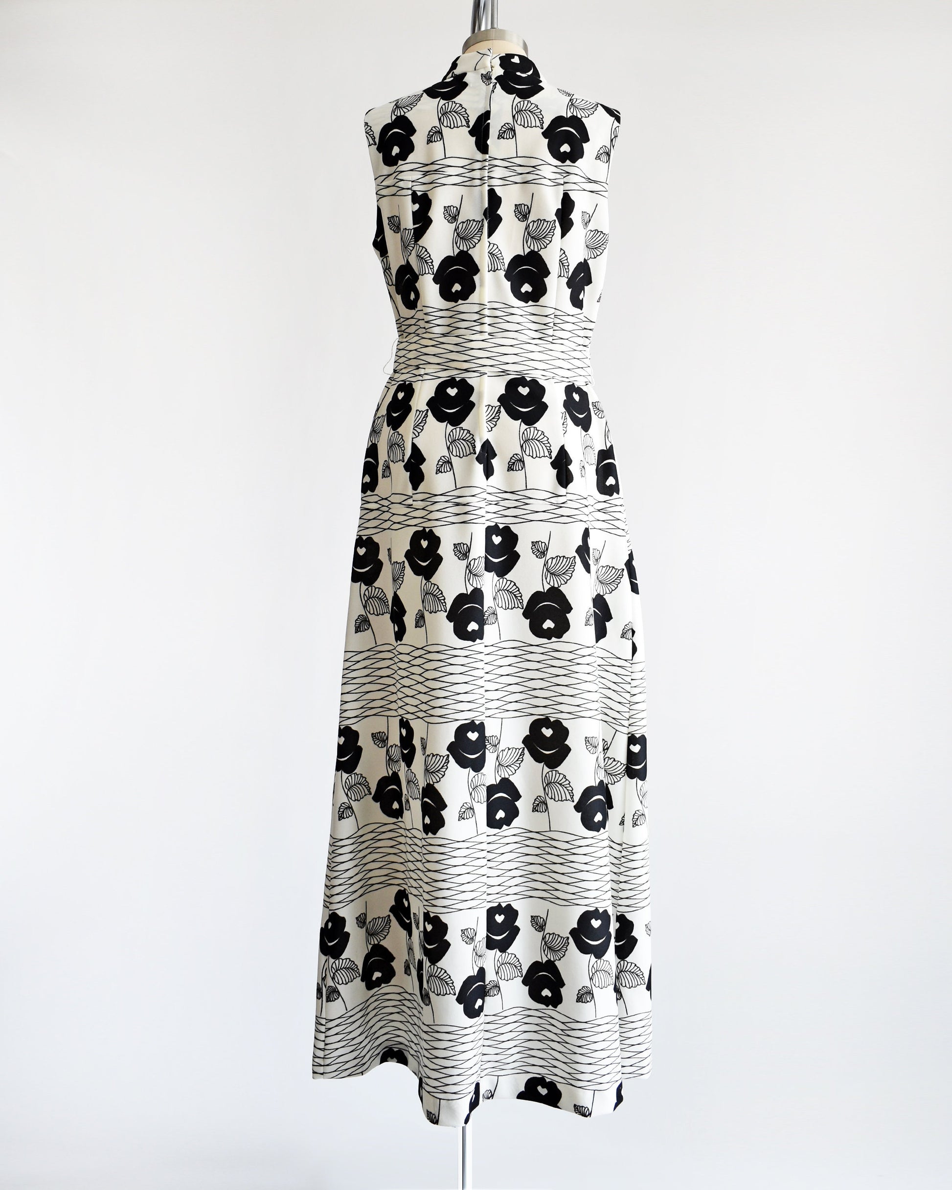Back view of a vintage 70s white maxi dress black floral print with wavy horizontal lines. Zipper up the back and matching belt.