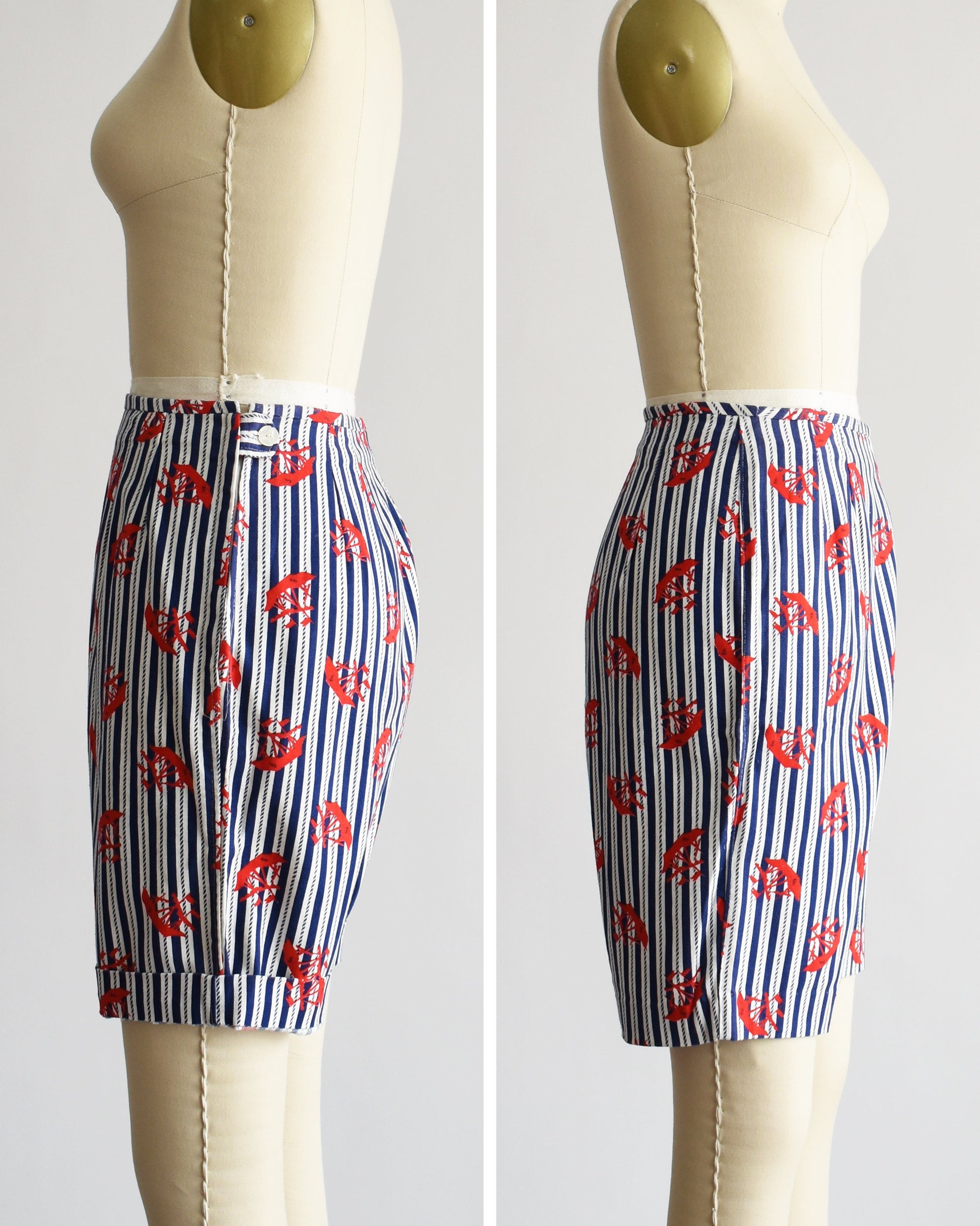 Side by side view of a pair of vintage 60s shorts that are navy blue and white vertical striped with a red clipper ship print. The shorts are modeled on a dress form. The shorts are cuffed on the left and not on the right.