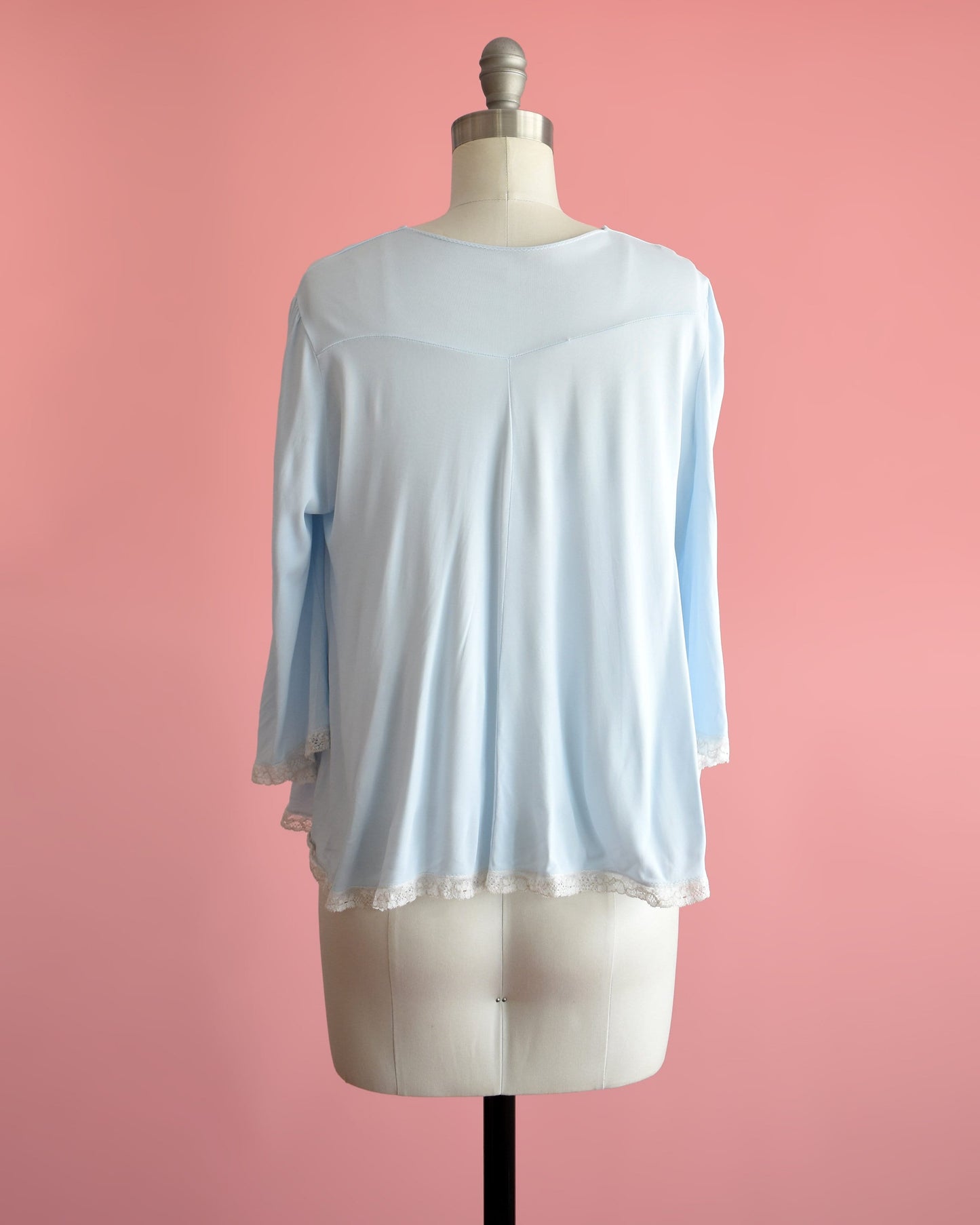 Back view of a vintage 60s light blue bed jacket with cream lace trim around the hem and cuffs. The garment is modeled on a dress form.