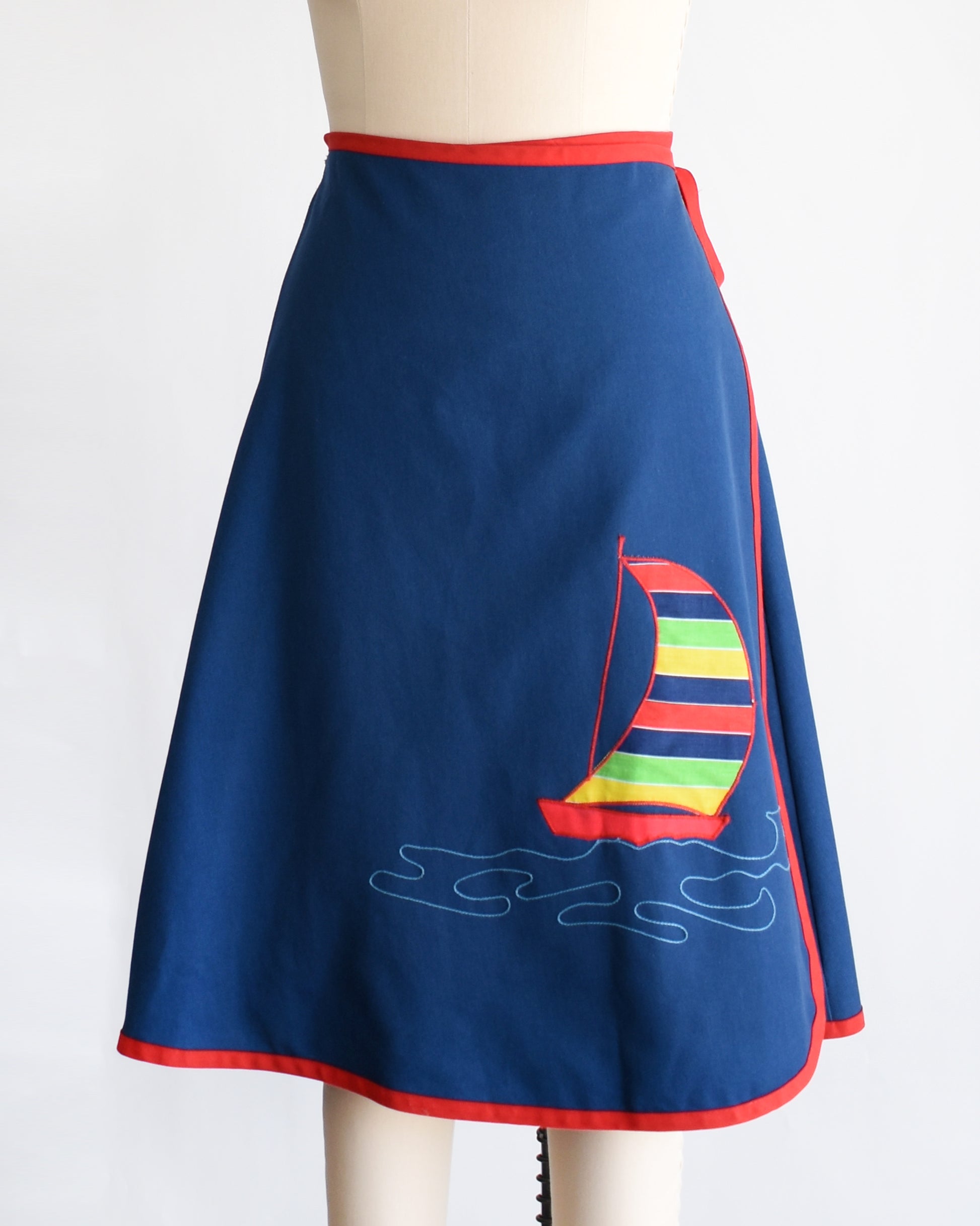 side front view of a vintage blue wrap skirt with a colorful sailboat design on a mannequin against a white background