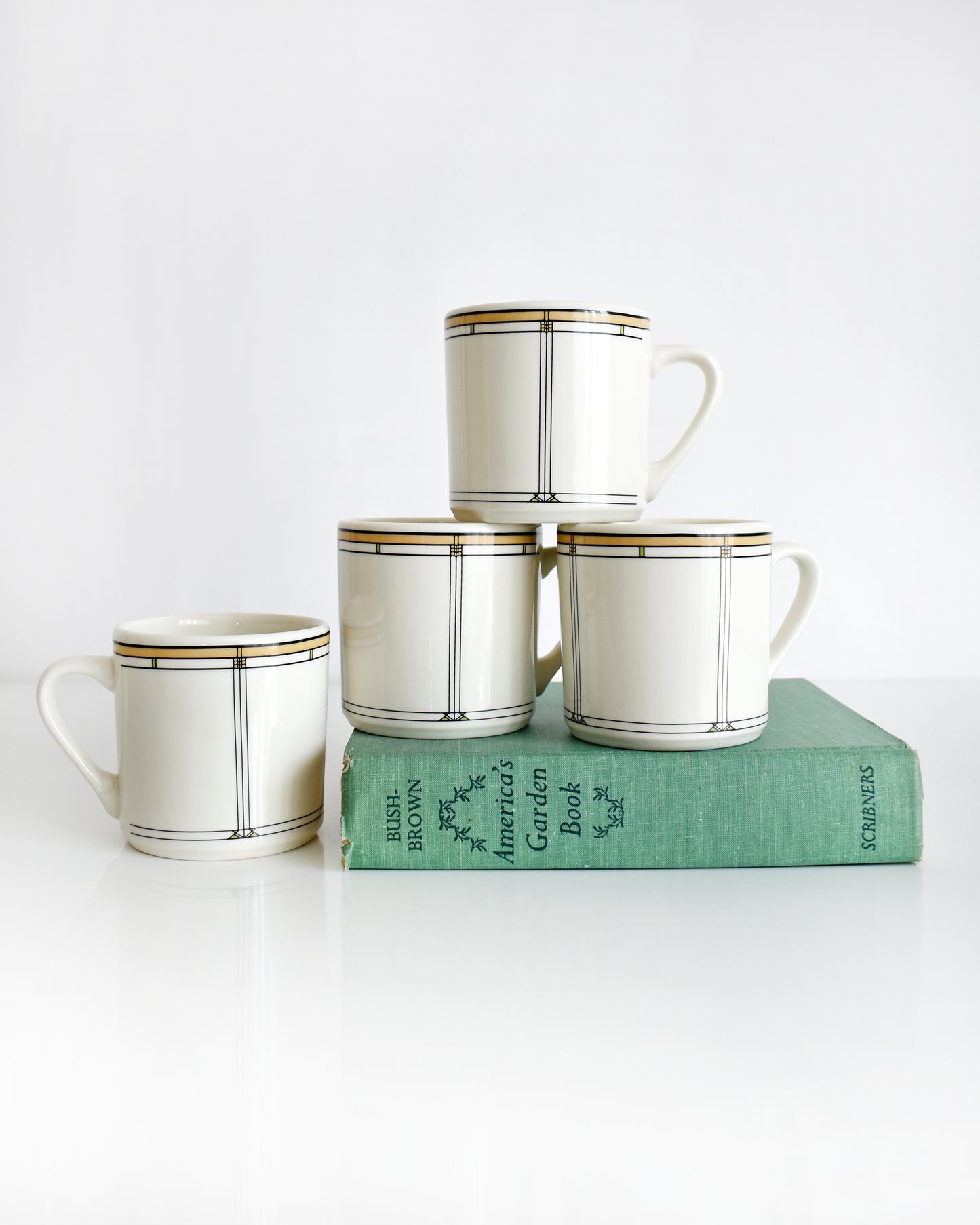 Set of four vintage Frank Lloyd Wright Martin House white mugs with gold trim on a white background