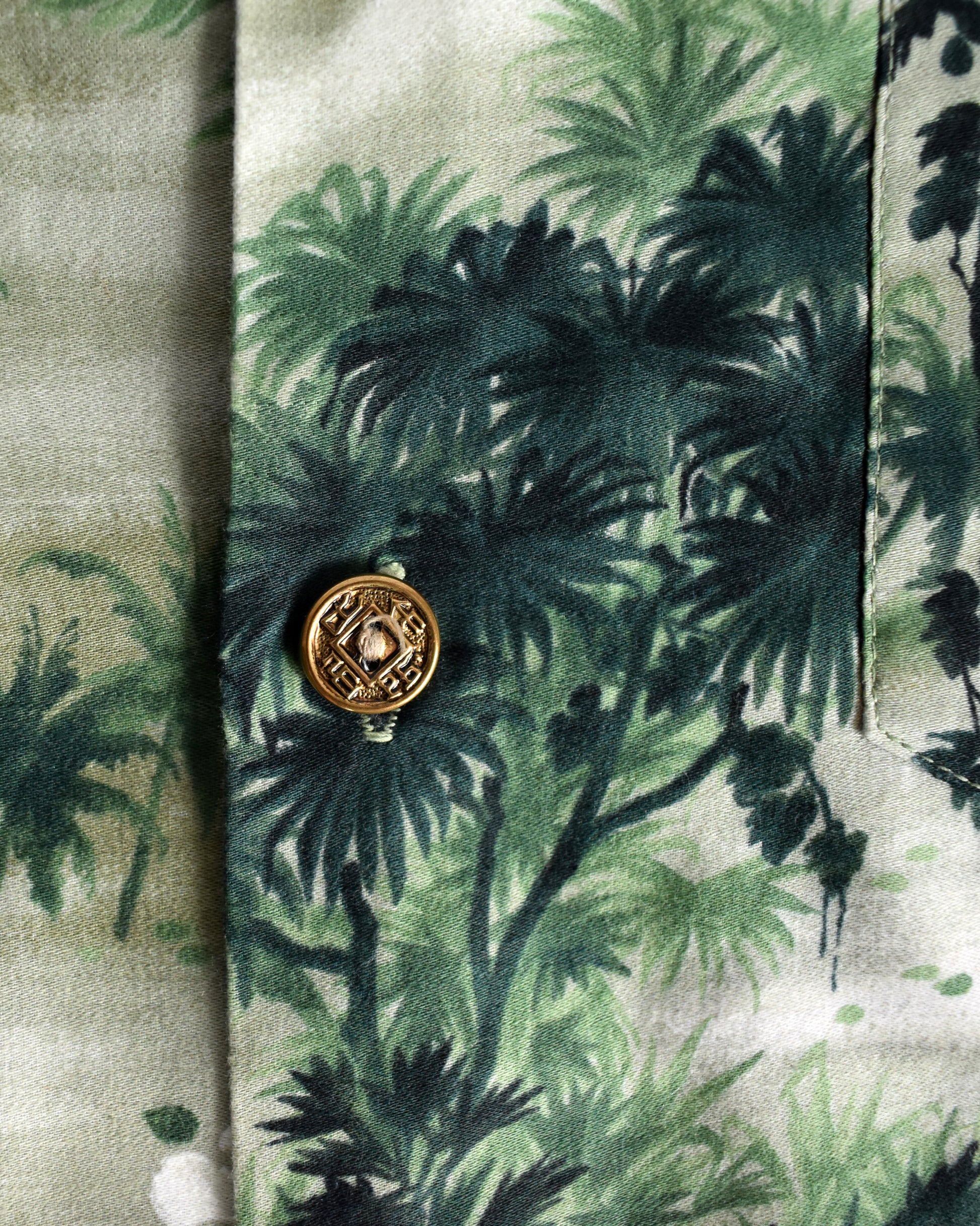 close up of the gold tone buttons on a vintage 1950s green Hawaiian shirt by Royal Hawaiian on a white background