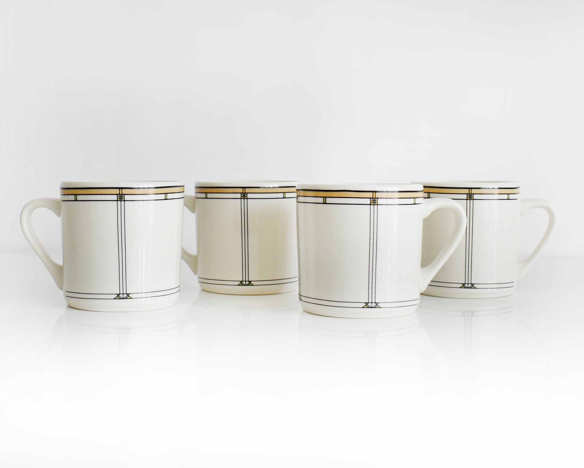 Set of four vintage Frank Lloyd Wright Martin House white mugs with gold trim on a white background