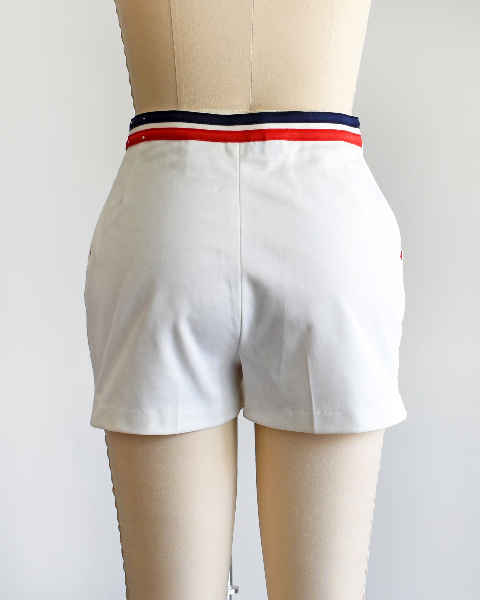 back view of a vintage 1970s white tennis shorts on a dress form. The shorts have red and blue bands along the waist on the back