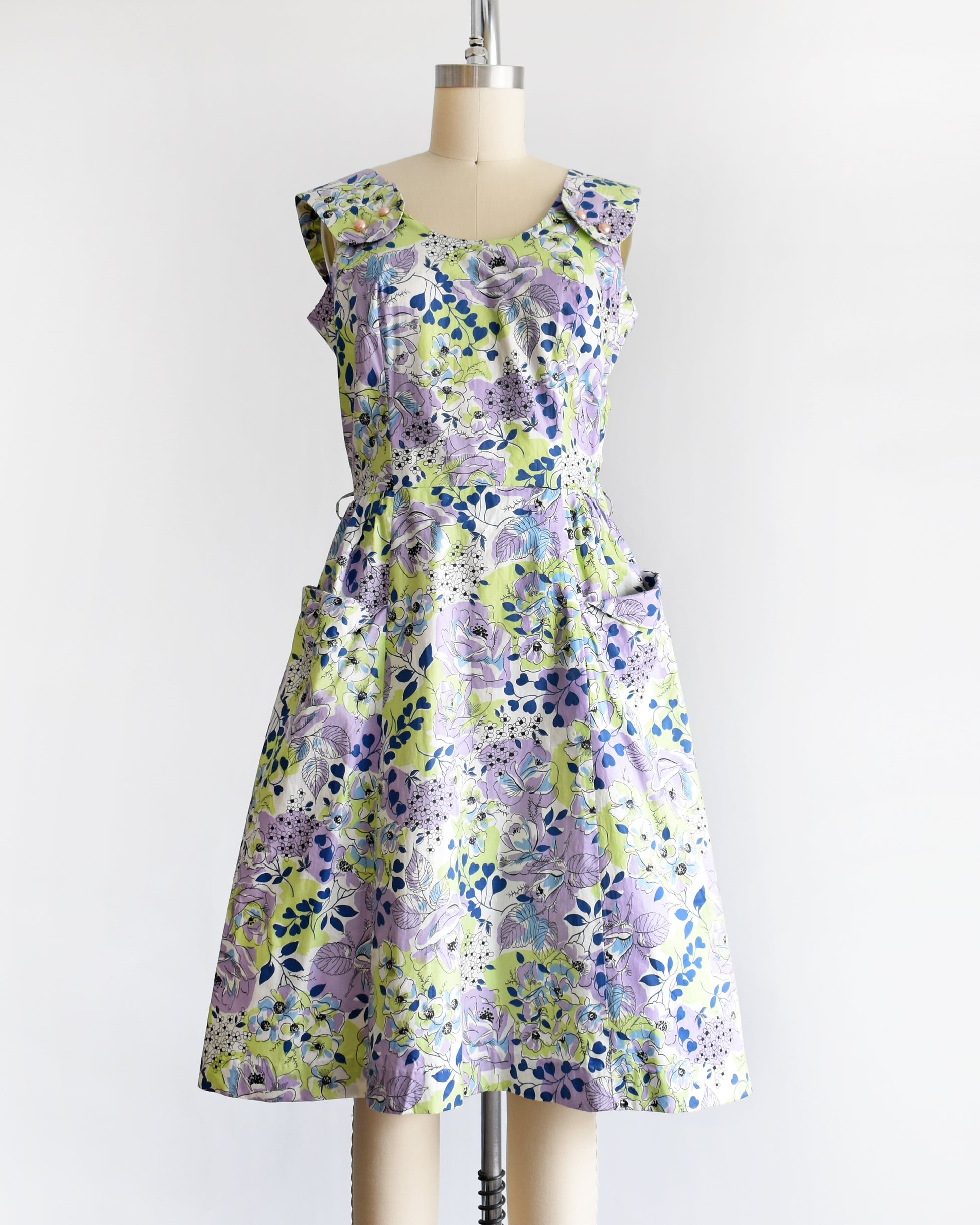 A vintage 1950s purple, green, blue, and white floral cotton sundress on a dress form