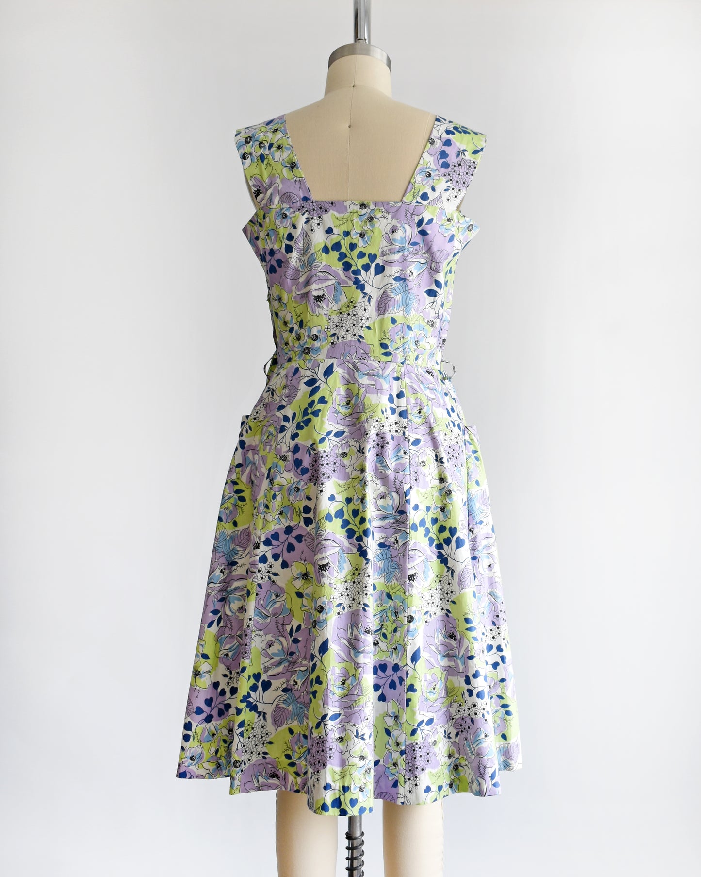 back view of a vintage 1950s purple, green, blue, and white floral cotton sundress on a dress form