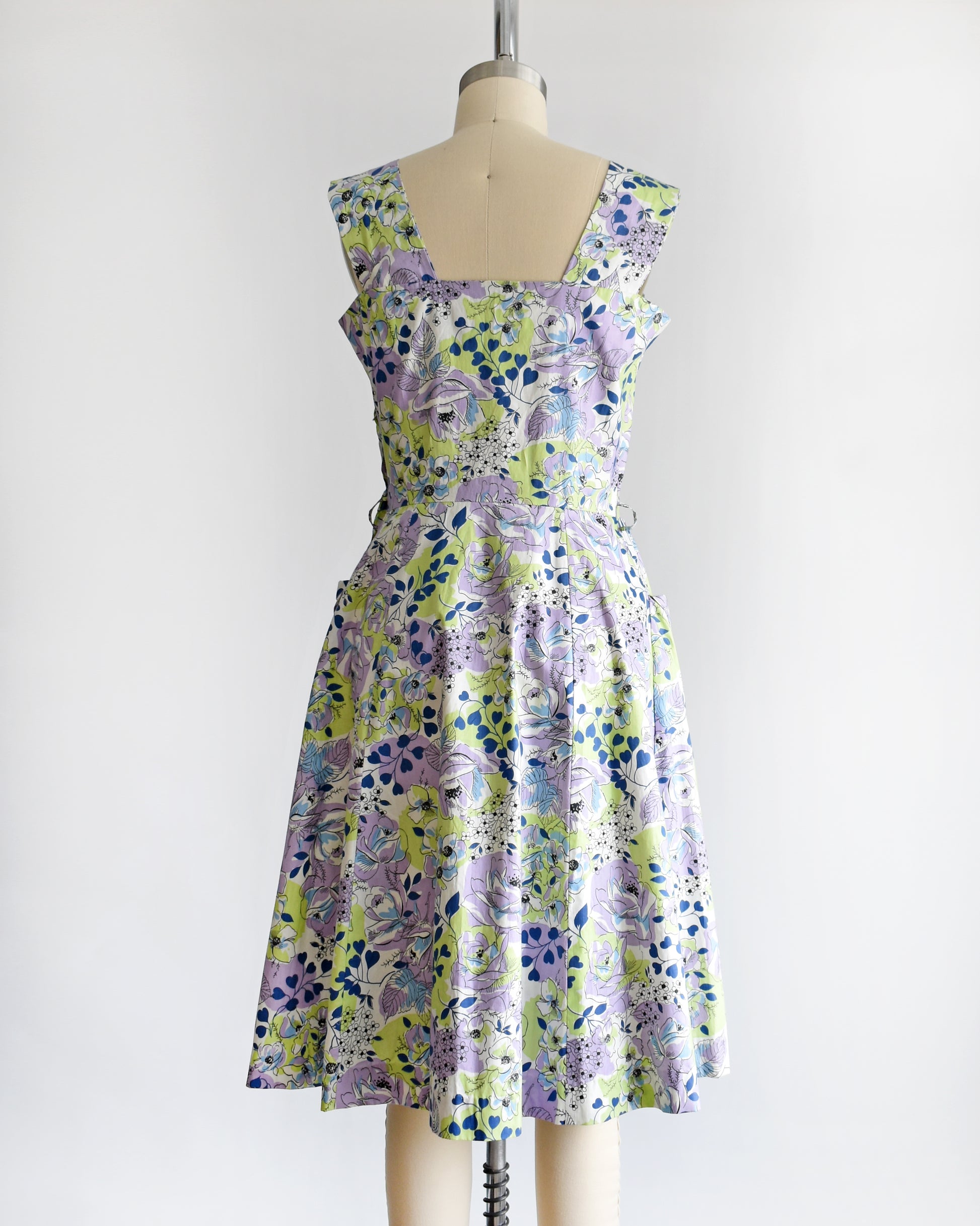 back view of a vintage 1950s purple, green, blue, and white floral cotton sundress on a dress form