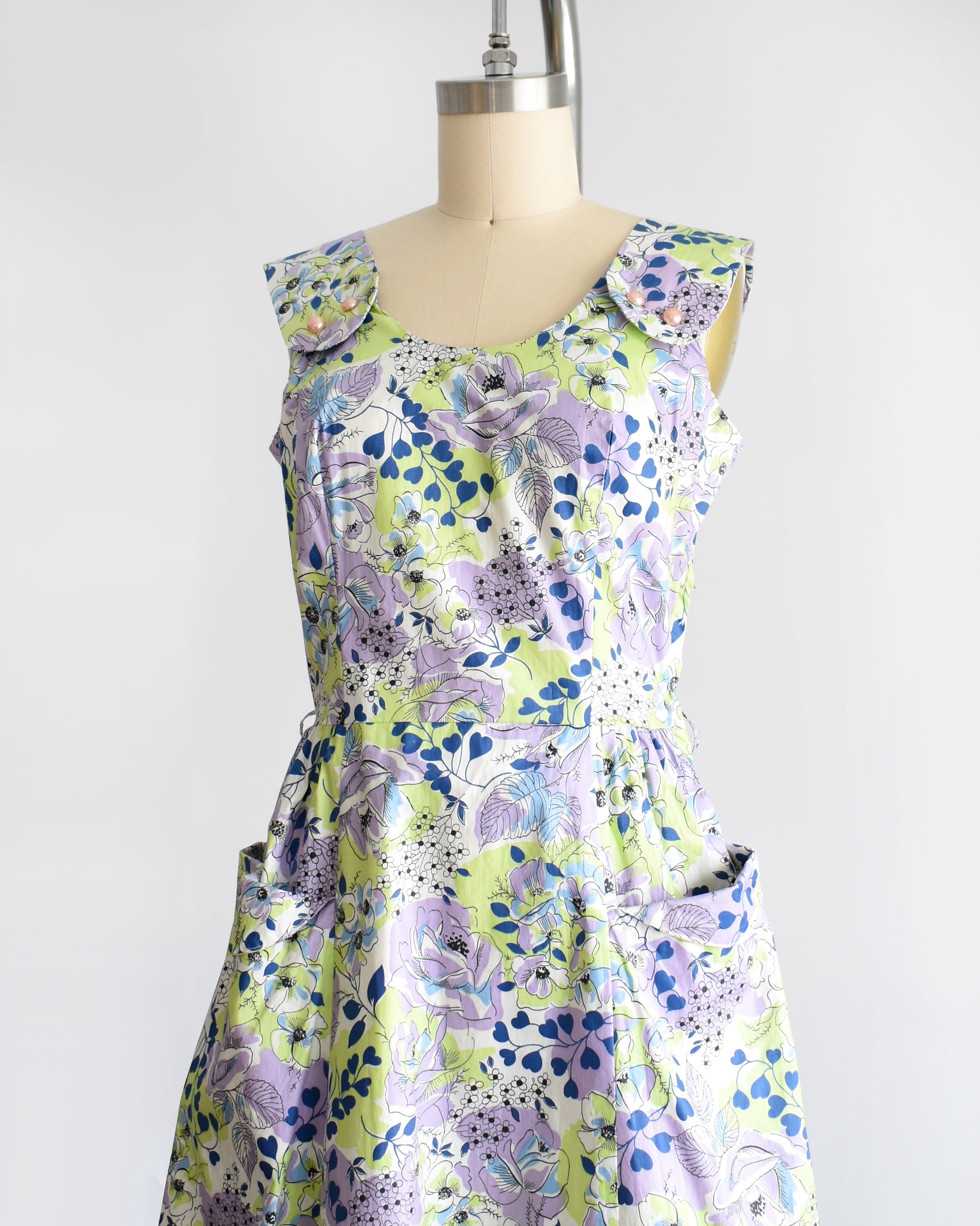 side front view of a vintage 1950s purple, green, blue, and white floral cotton sundress on a dress form