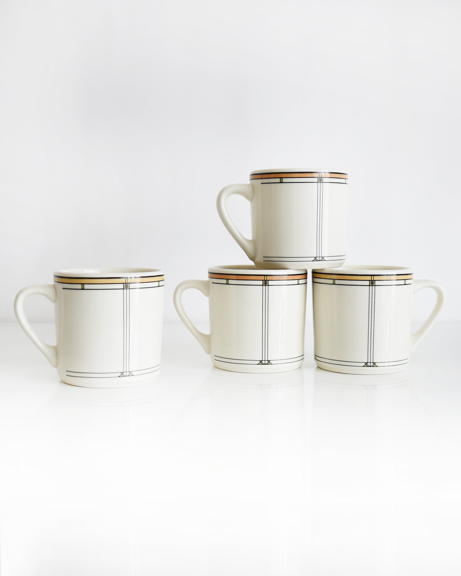 Set of four vintage Frank Lloyd Wright Martin House white mugs with gold trim on a white background