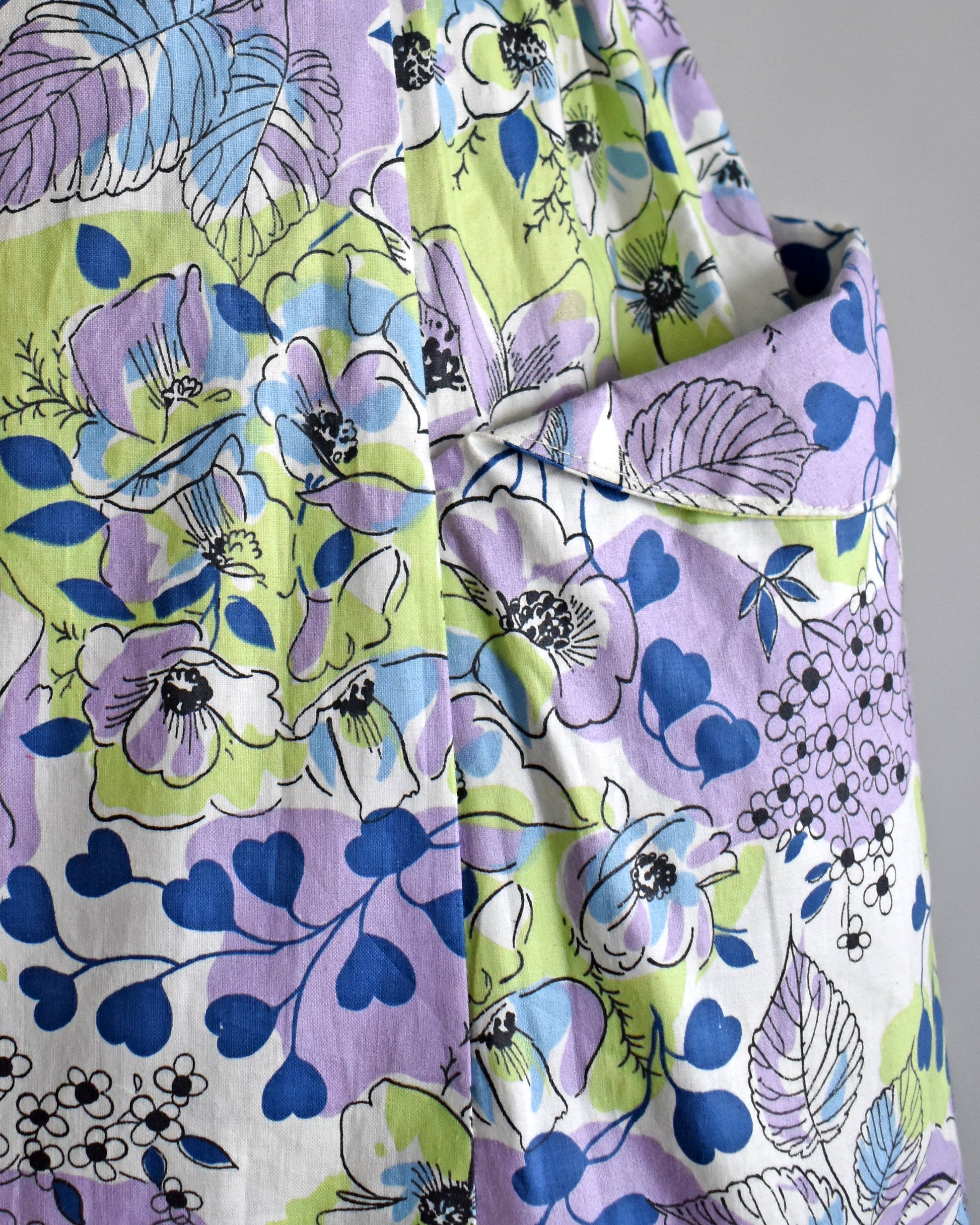 close up of a pocket on a vintage 1950s purple, green, blue, and white floral cotton sundress on a dress form