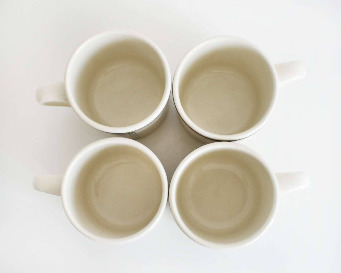 overhead shot of a set of four vintage Frank Lloyd Wright Martin House white mugs with gold trim on a white background
