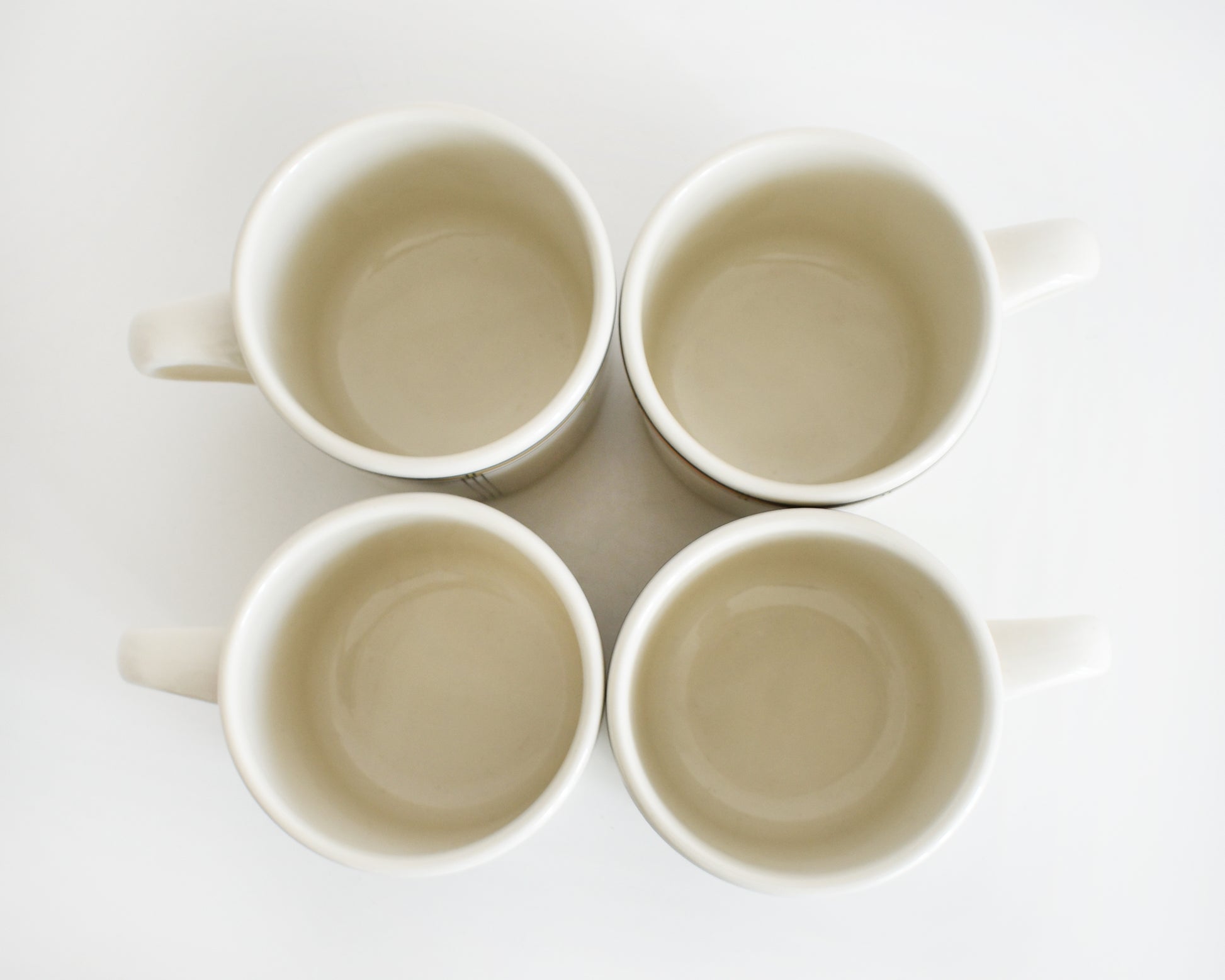 overhead shot of a set of four vintage Frank Lloyd Wright Martin House white mugs with gold trim on a white background