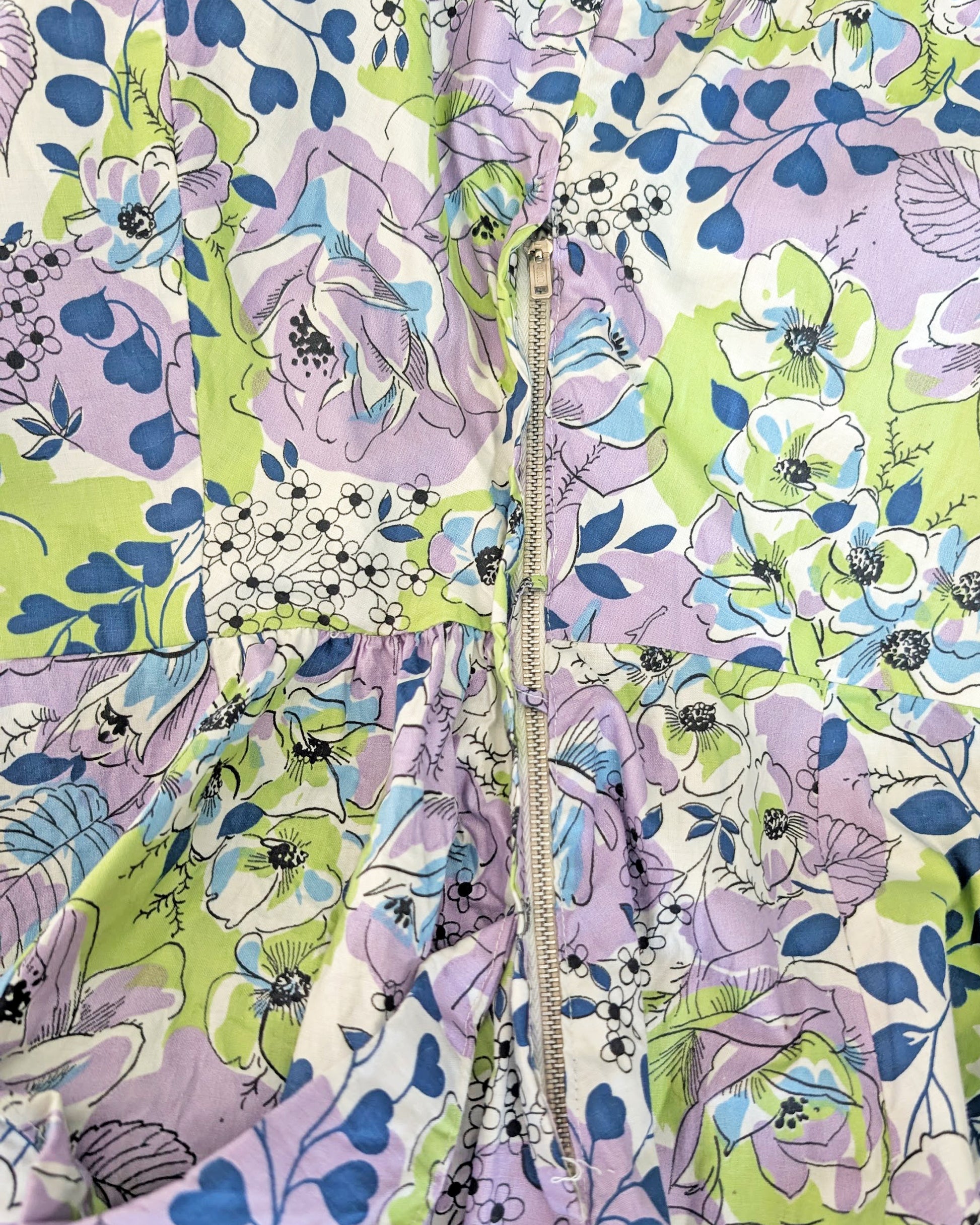 close up of the metal zipper on a vintage 1950s purple, green, blue, and white floral cotton sundress on a dress form