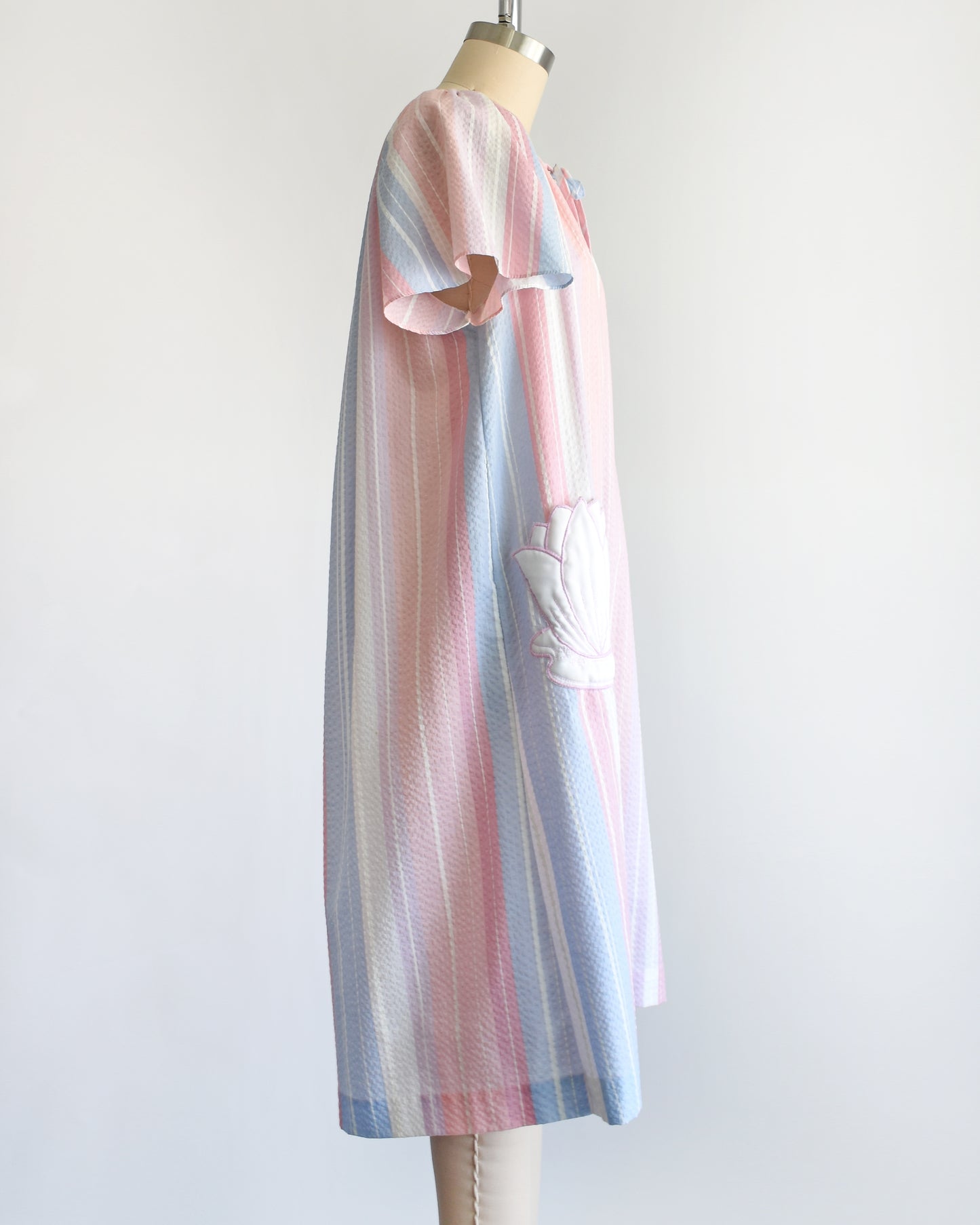 side view of a vintage 1980s blue, pink, and white striped house dress with a white lily pad pocket on a dress form