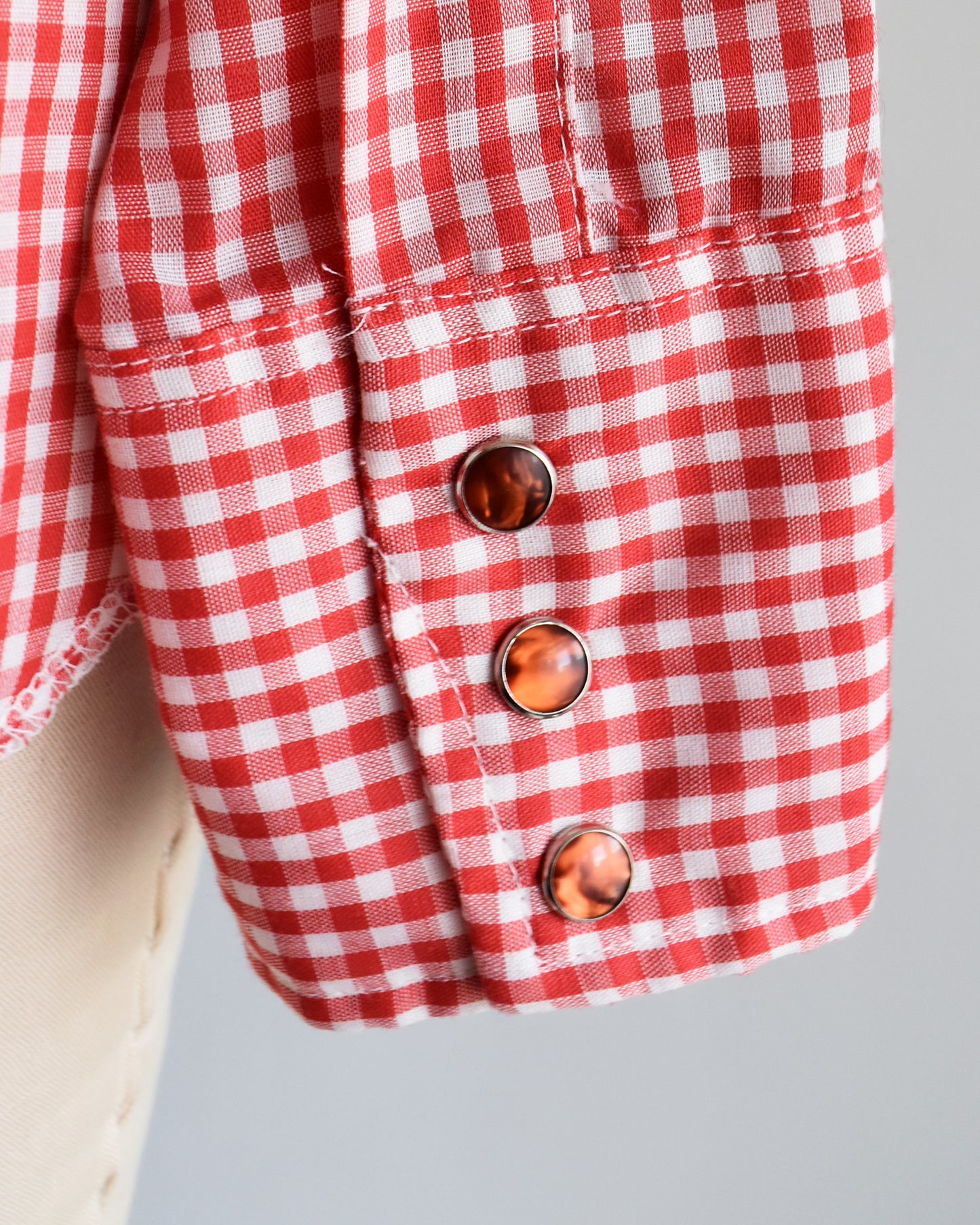 close up of the red pearl snaps on the cuff of a vintage 1970s red and white gingham shirt on a mannequin against a white background