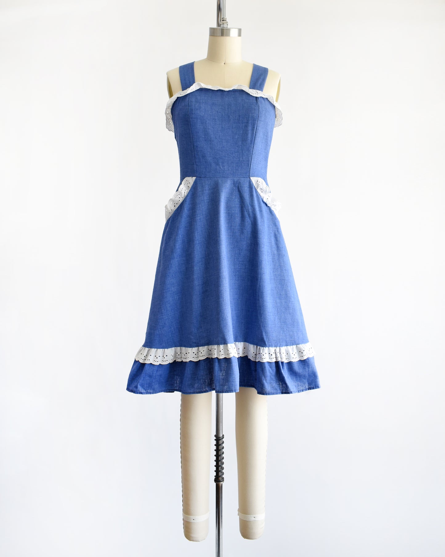 a vintage 1970s blue dress with white lace details on a mannequin against a white background