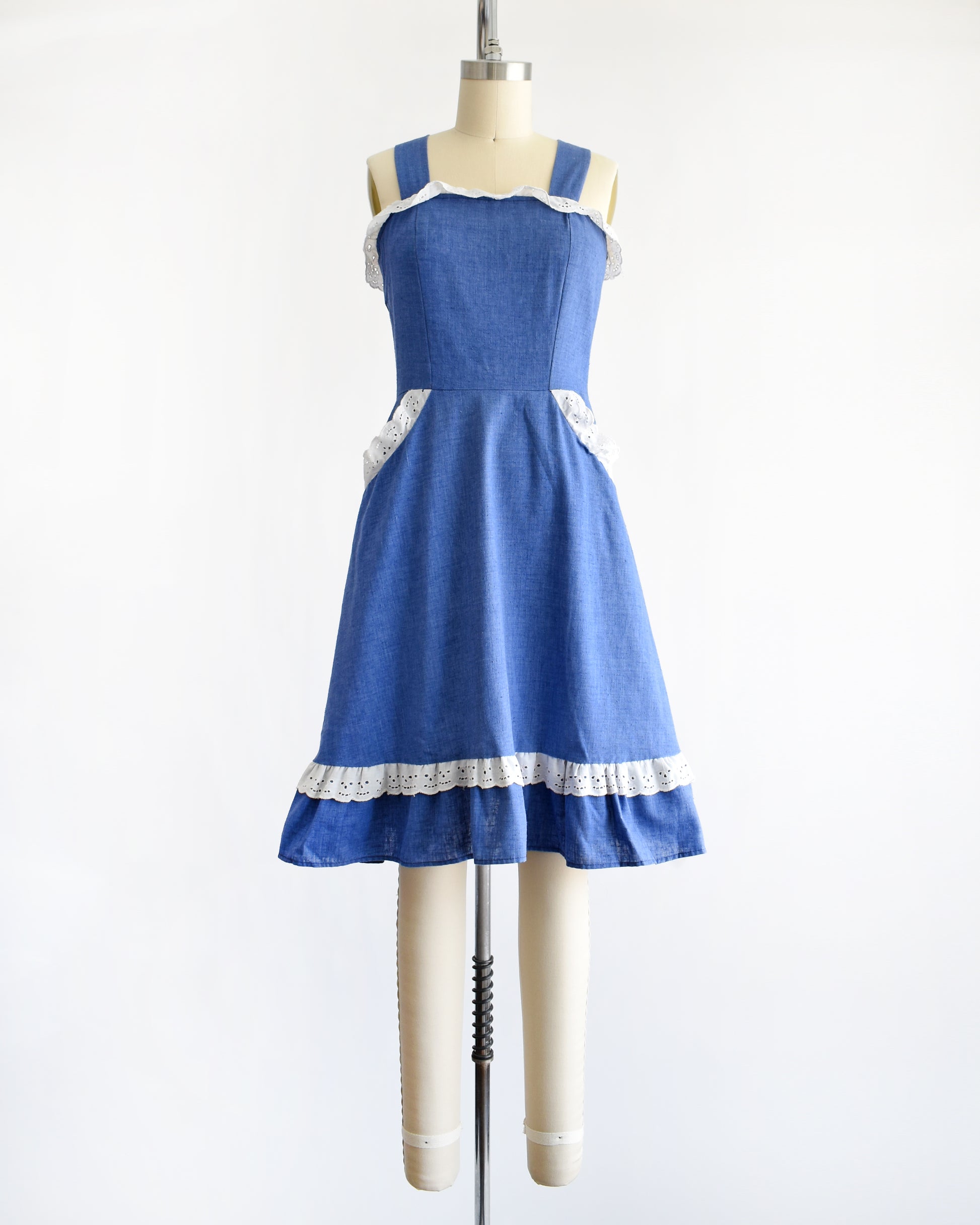 a vintage 1970s blue dress with white lace details on a mannequin against a white background