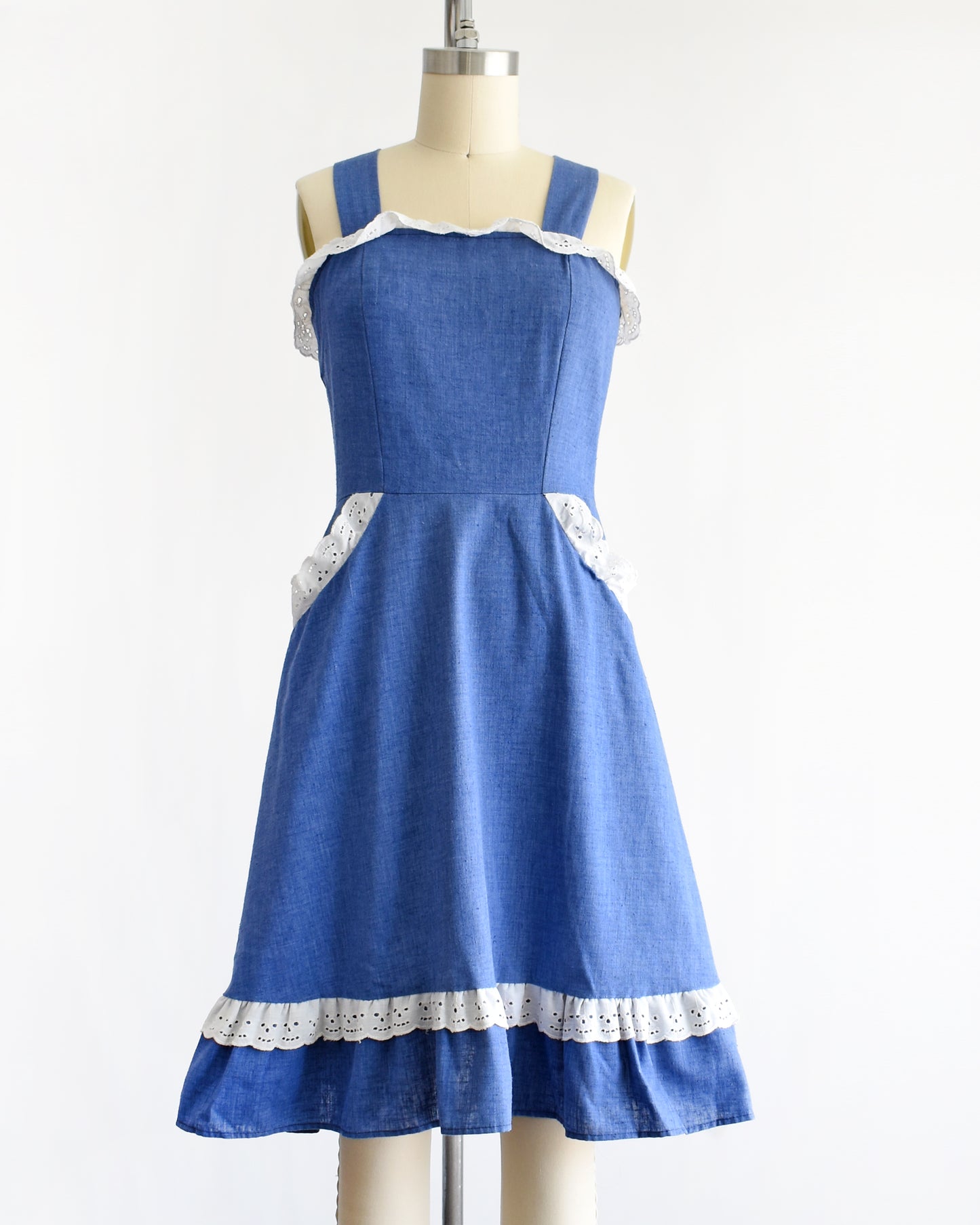 a vintage 1970s blue dress with white lace details on a mannequin against a white background