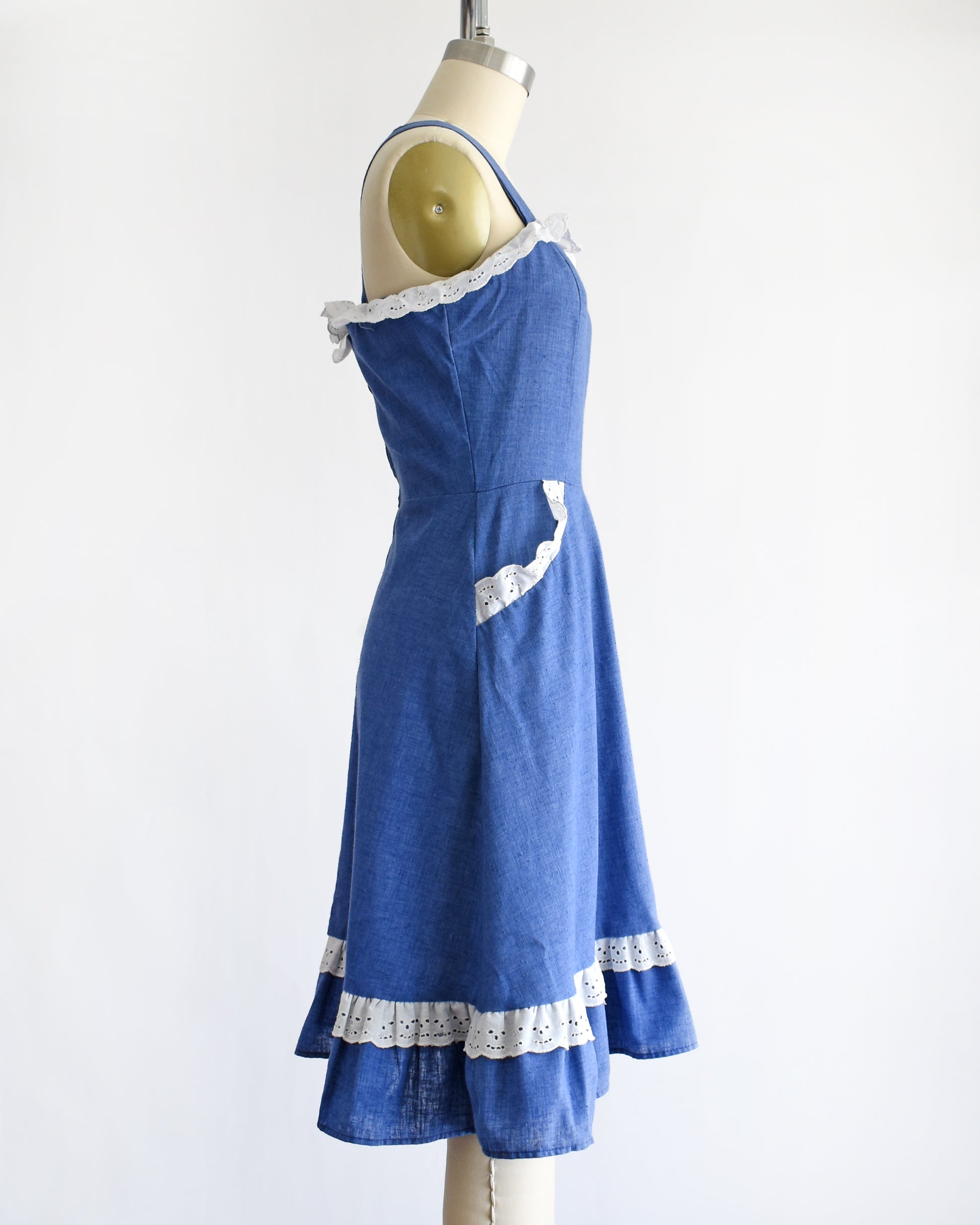 side view of a vintage 1970s blue dress with white lace details on a mannequin against a white background