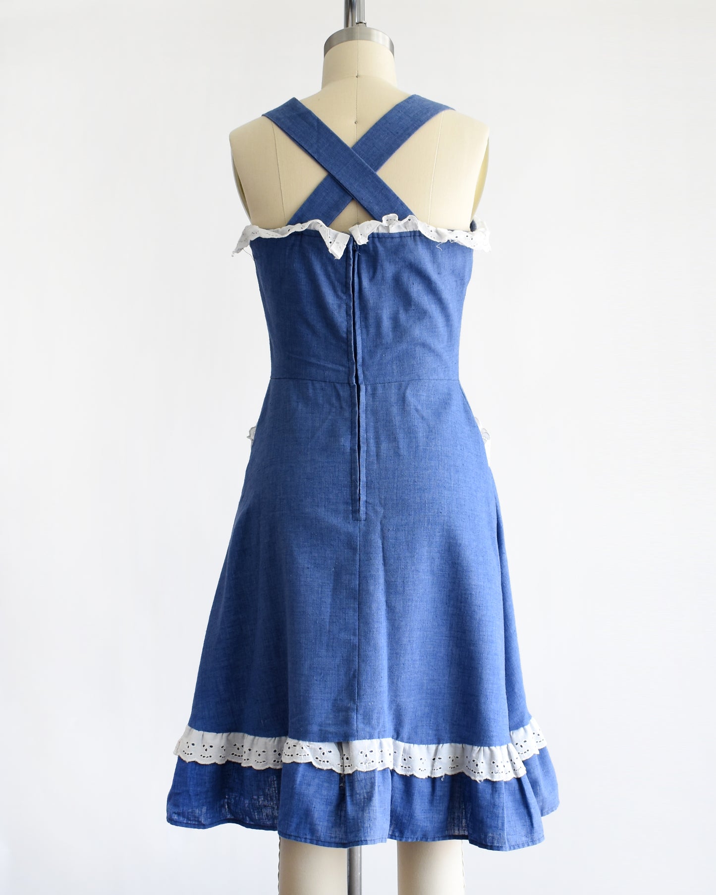 back view of a vintage 1970s blue dress with white lace details on a mannequin against a white background