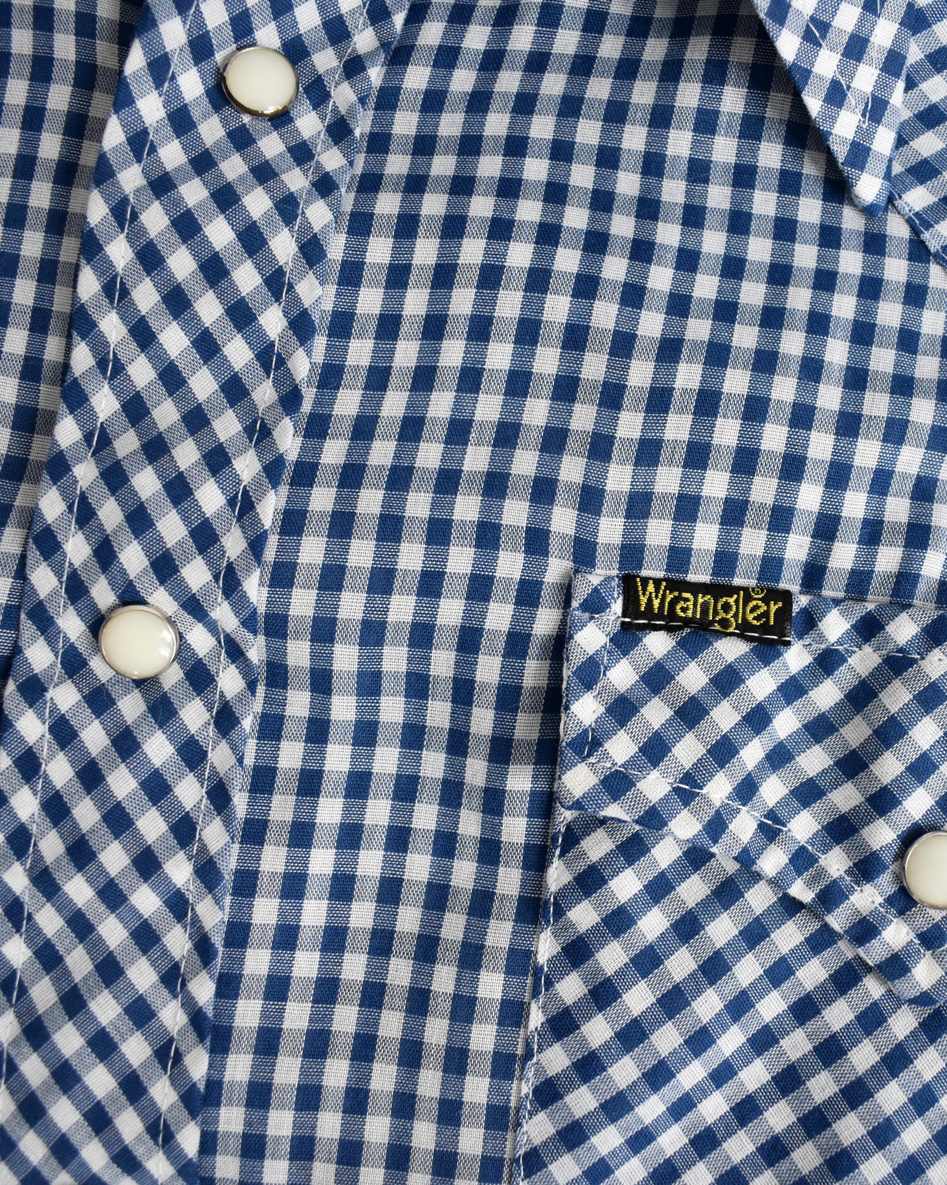 Close-up of a blue and white checkered shirt with a Wrangler logo on the chest pocket.