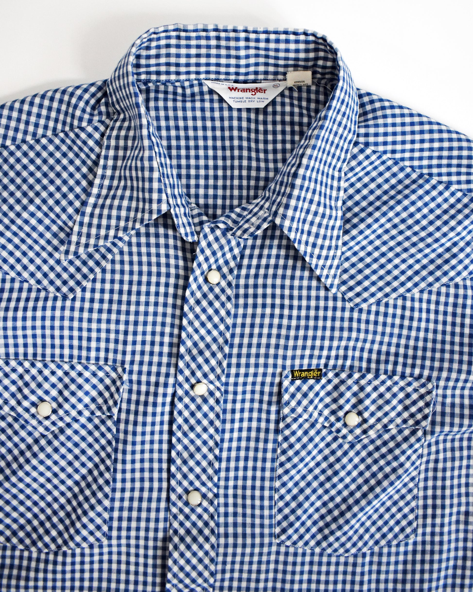 close up o the collar and front pockets on a  vintage 1980s blue checkered pearl snap Wrangler shirt on a white background