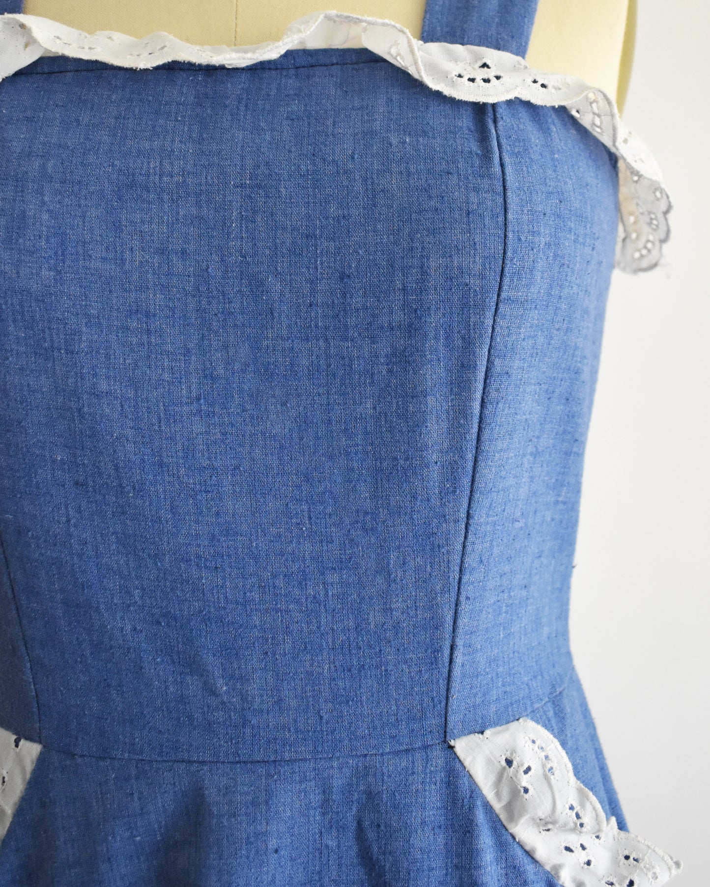 close up of the bodice of a vintage 1970s blue dress with white lace details on a mannequin against a white background