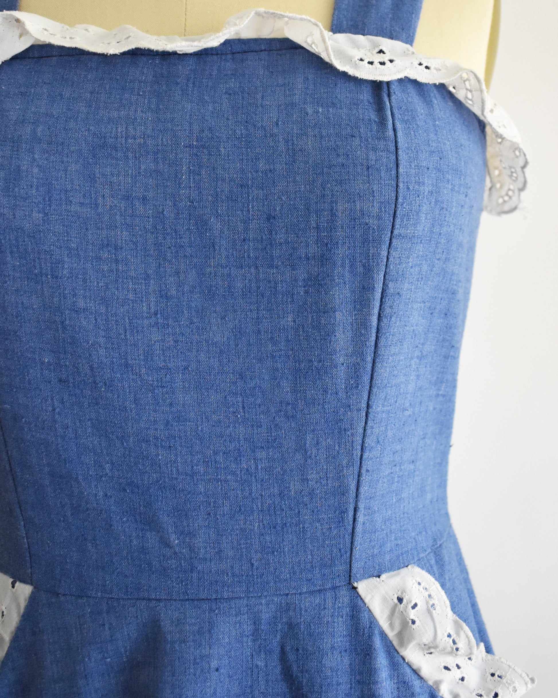 close up of the bodice of a vintage 1970s blue dress with white lace details on a mannequin against a white background