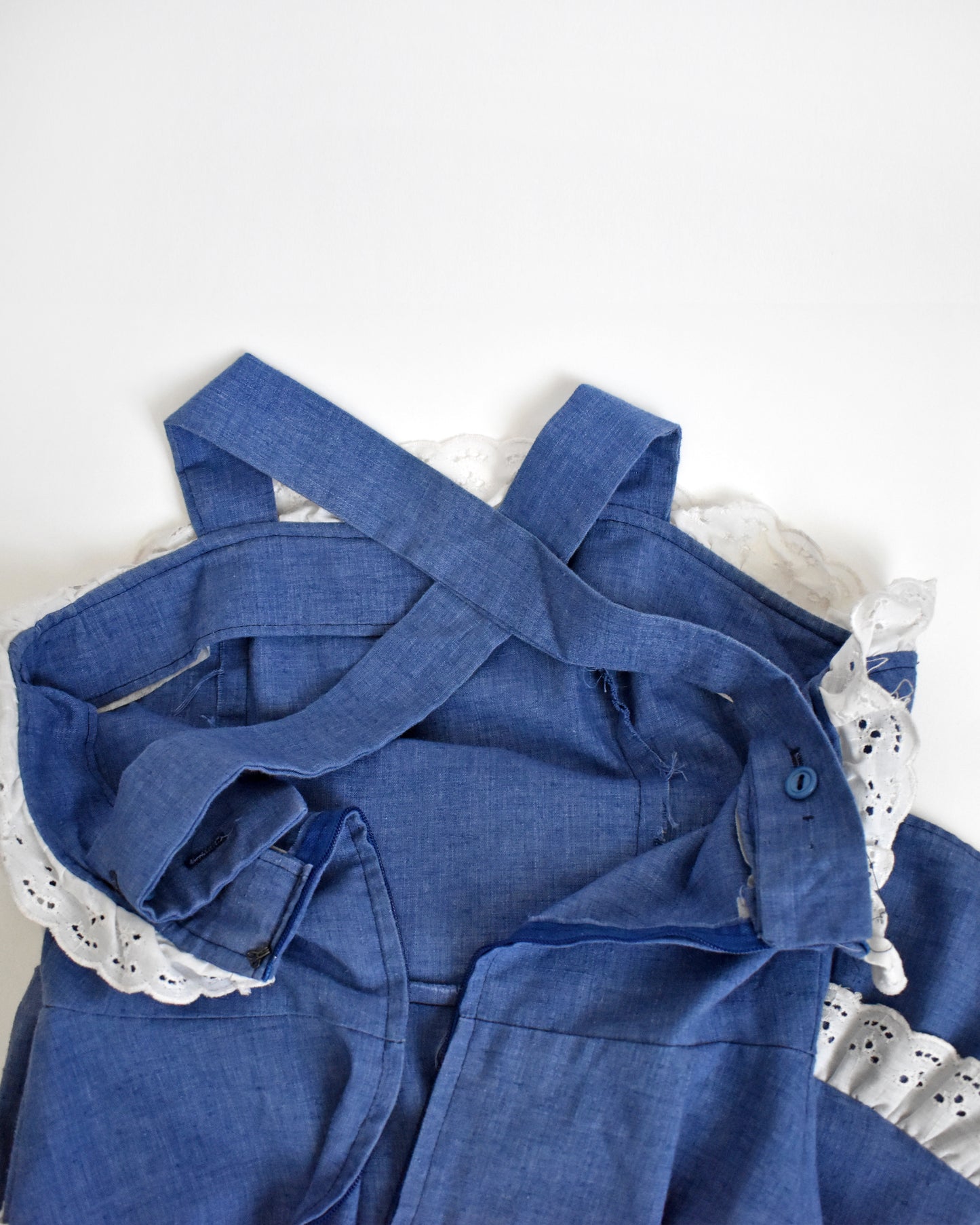 flat lay view of the criss cross straps on the back of a vintage 1970s blue dress with white lace details on a mannequin against a white background
