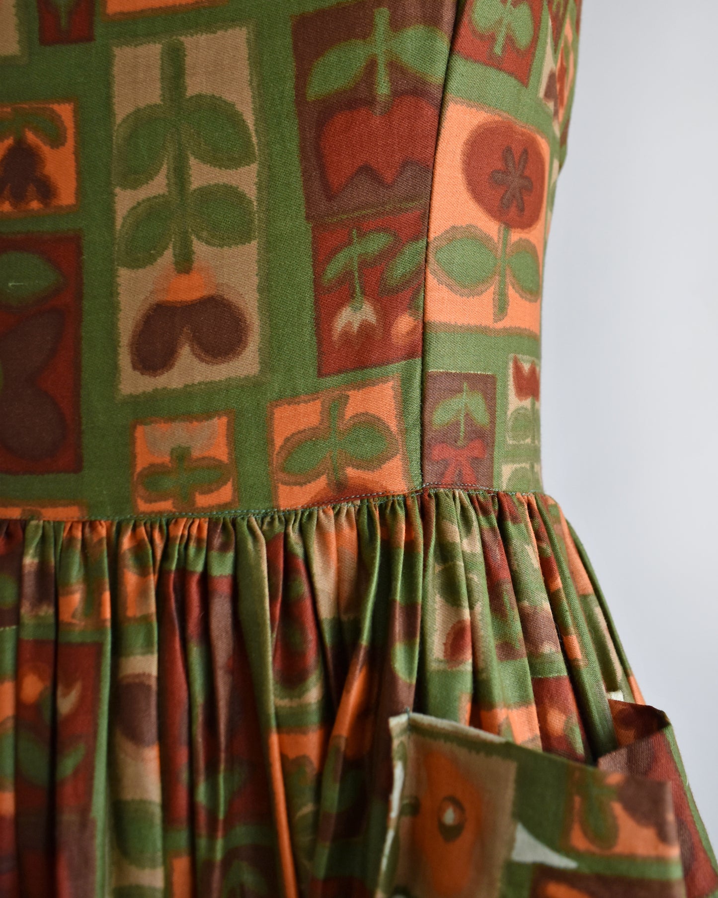 close up of the waist of a vintage 1960s fruits and florals patterned dress on a mannequin against a white background