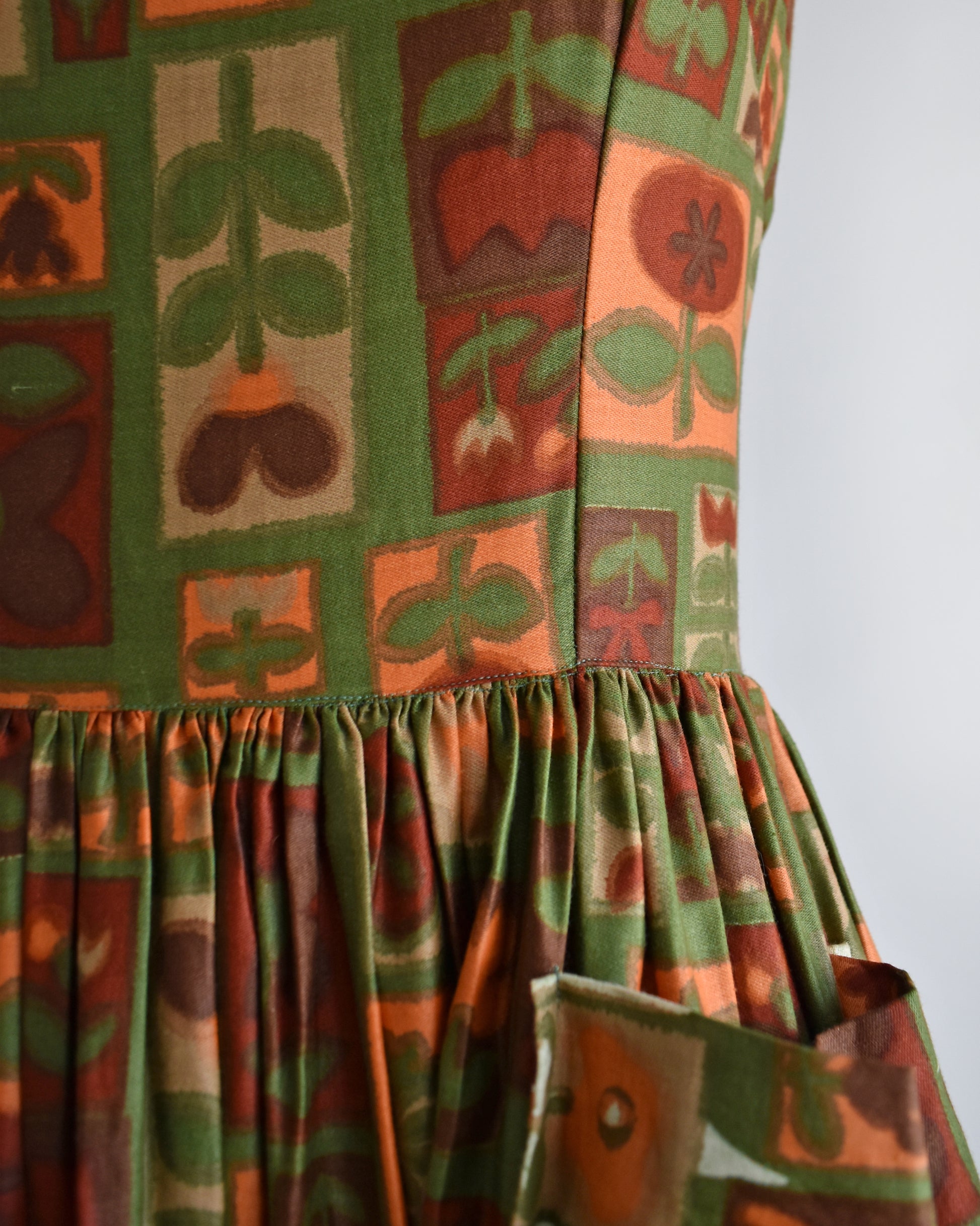 close up of the waist of a vintage 1960s fruits and florals patterned dress on a mannequin against a white background